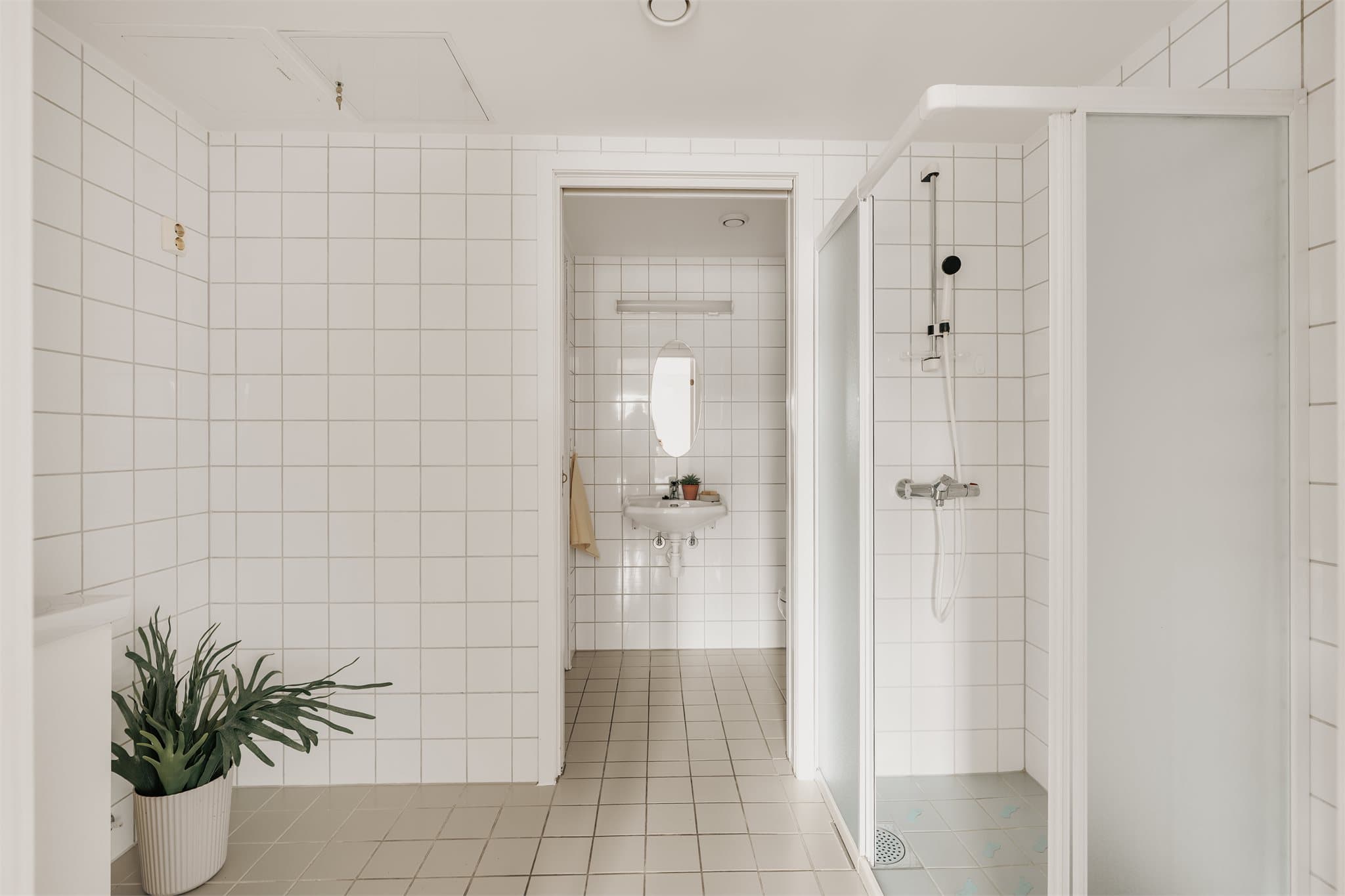 Rommet er utstyrt med servant med heldekkende servantplate og underskap med glatte fronter, samt speil med tilhørende lysarmatur montert på vegg. Det er gulvmontert toalett og dusjhjørne med skyvedører, håndholdt dusj og termostatstyrt blandebatteri.