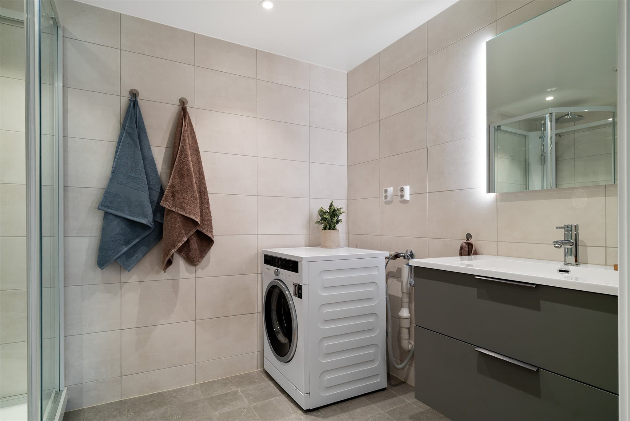 Lekkert, flislagt bad med opplegg for vaskemaskin og tørketrommel.