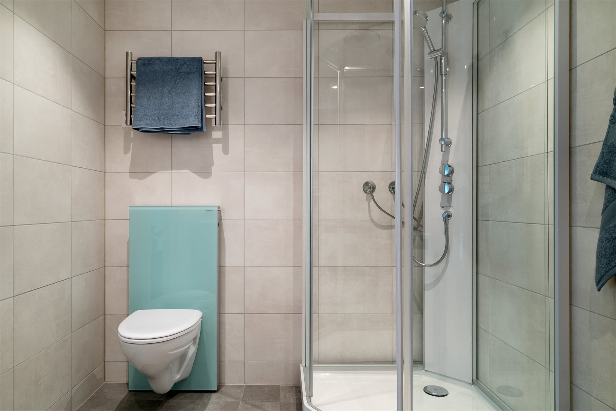 Badet er utstyrt med dusjhjørne, vegghengt toalett og servant.