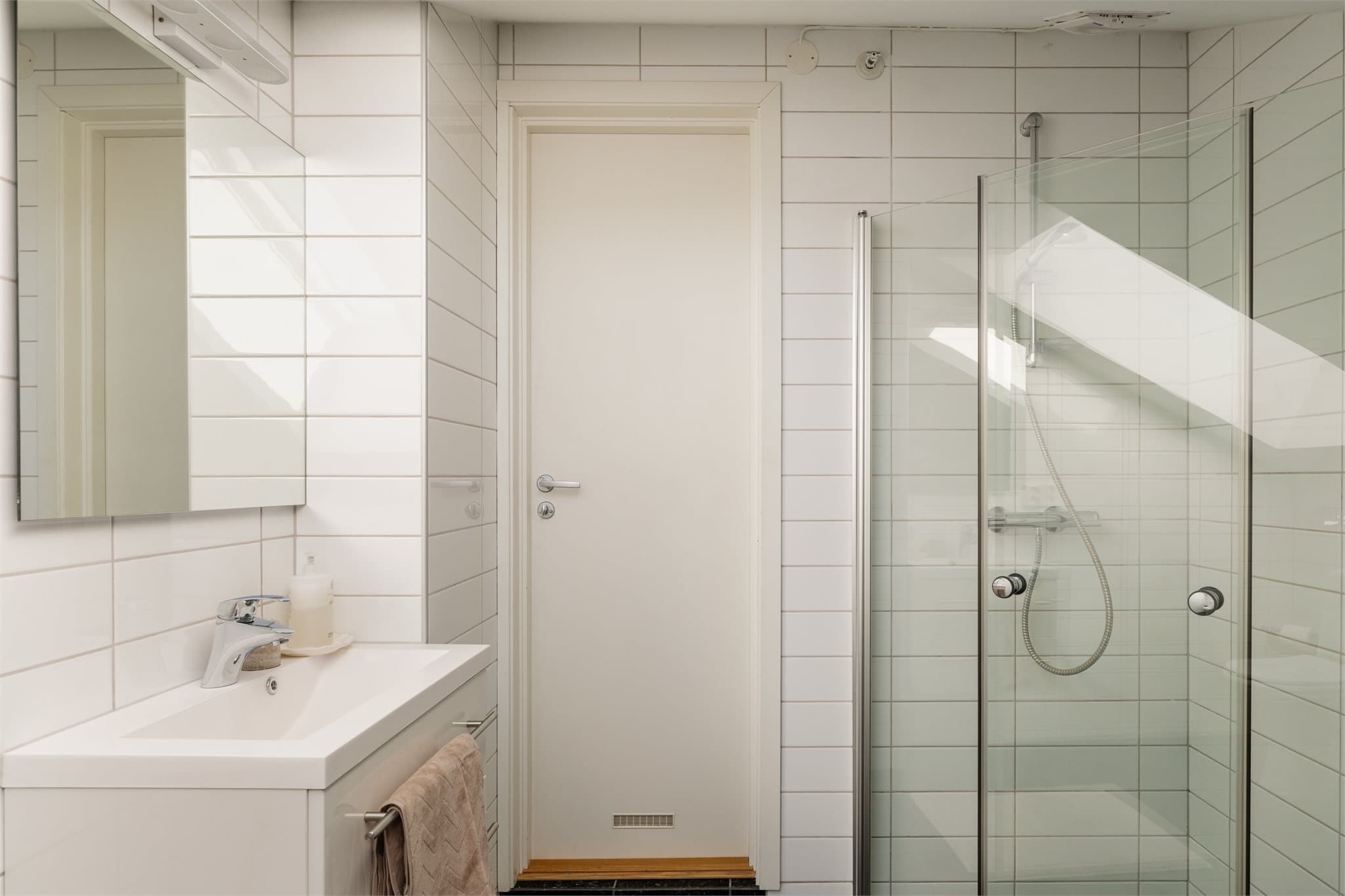 Badet har dusjhjørne med praktiske, innsvingbare dører og servant med skuffeinnredning.