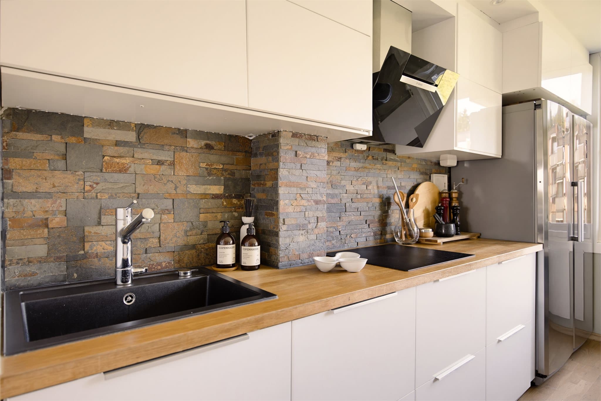 Kjøkkeninnredningen fra IKEA har stilrene, hvite høyglansfronter som kombineres med en heltre benkeplate. En lekker backsplash av skifer.