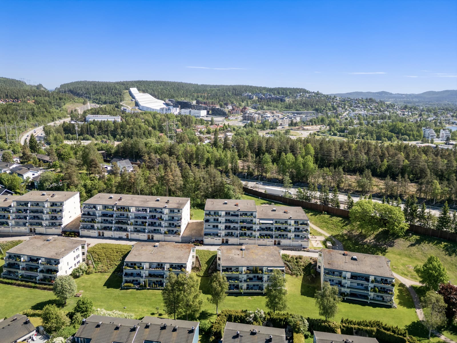 Fra området kan du nyte utsyn over grønne omgivelser og nærliggende bebyggelse. På flere av dronebildene skimtes også SNØ, som tilbyr helårs ski- og aktivitetsmuligheter.