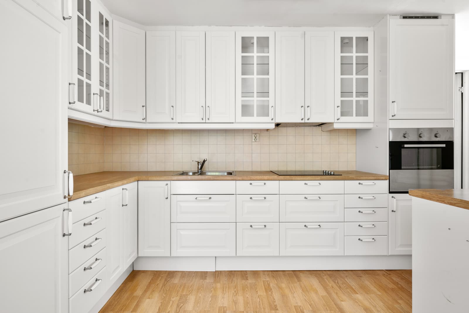Innredningen er fra IKEA (ca. 2012) og har hvite, profilerte fronter som gir et tidløst og klassisk uttrykk. Vitrineskapene tilfører et elegant preg og gir mulighet for å vise frem servise og glass på en dekorativ måte.