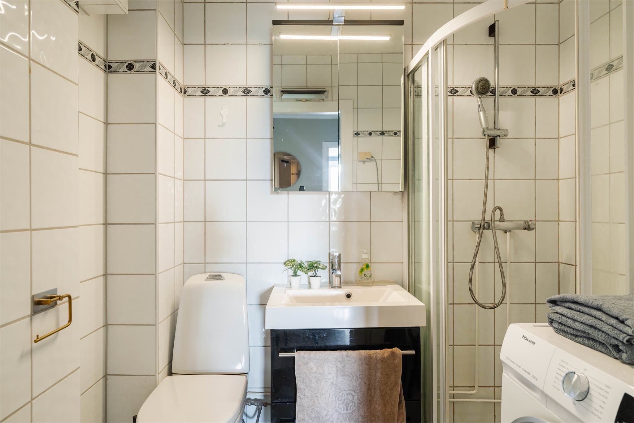Badet er utstyrt med dusjhjørne, servantskap og gulvmontert toalett.