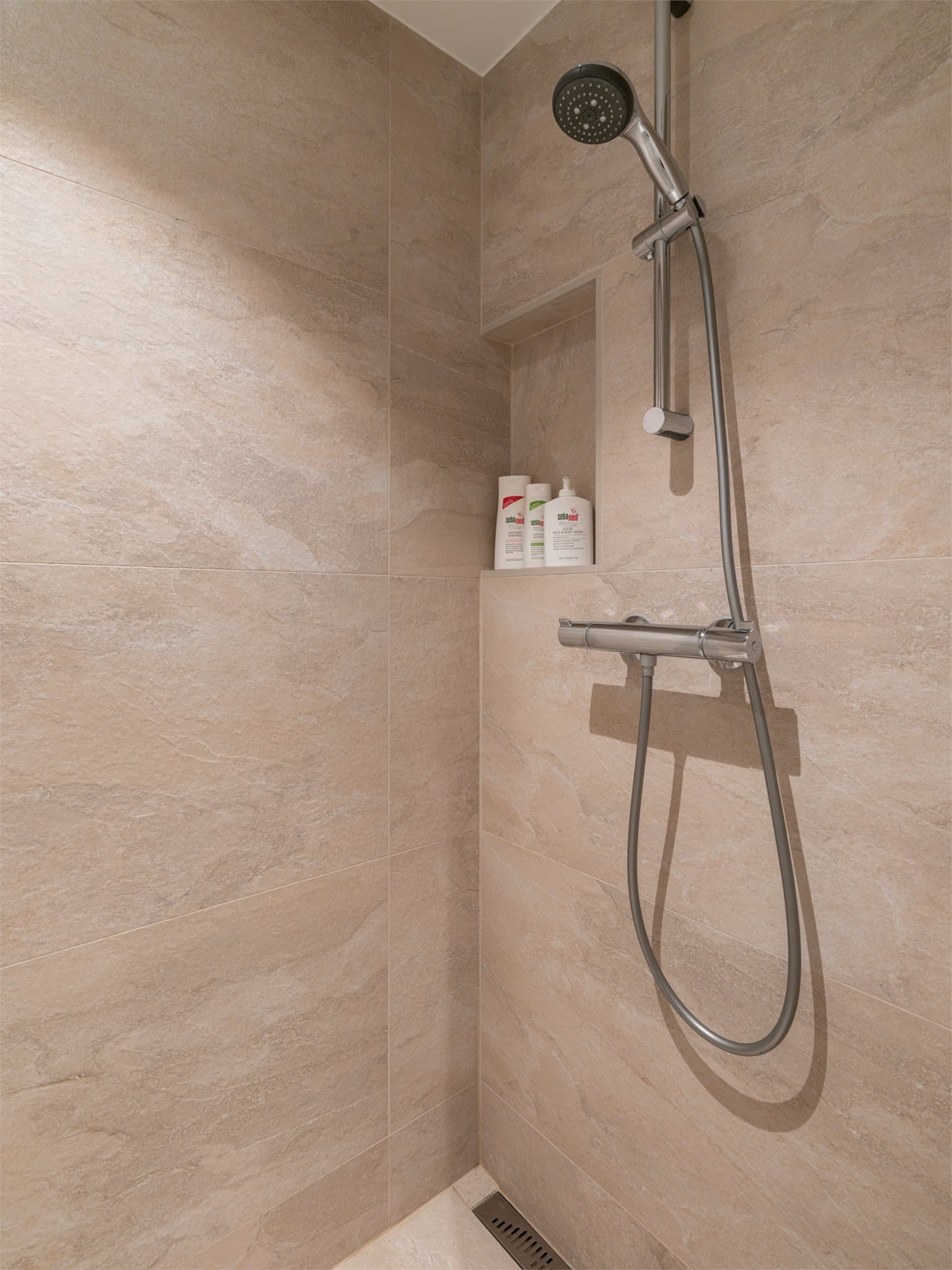 Dusjsonen har en praktisk nisje for oppbevaring og en moderne slukrenne.