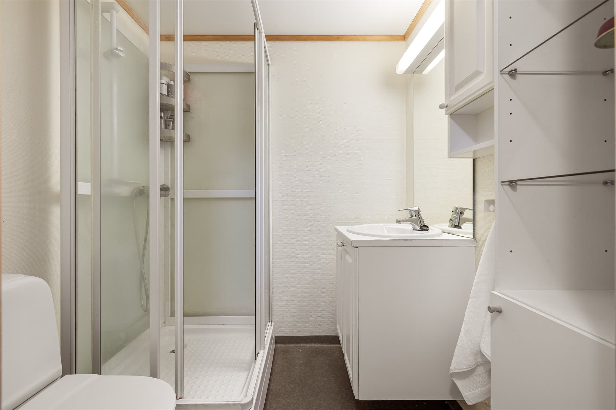Badet er innredet med dusjkabinett, toalett, servantinnredning, speil og gode oppbevaringsmuligheter i skap.