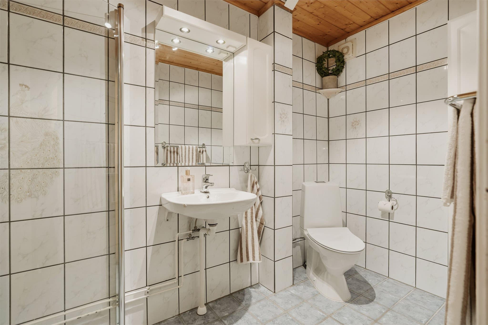 Det første badet ligger tilknyttet gangen. Det er fliser på gulv og vegger.