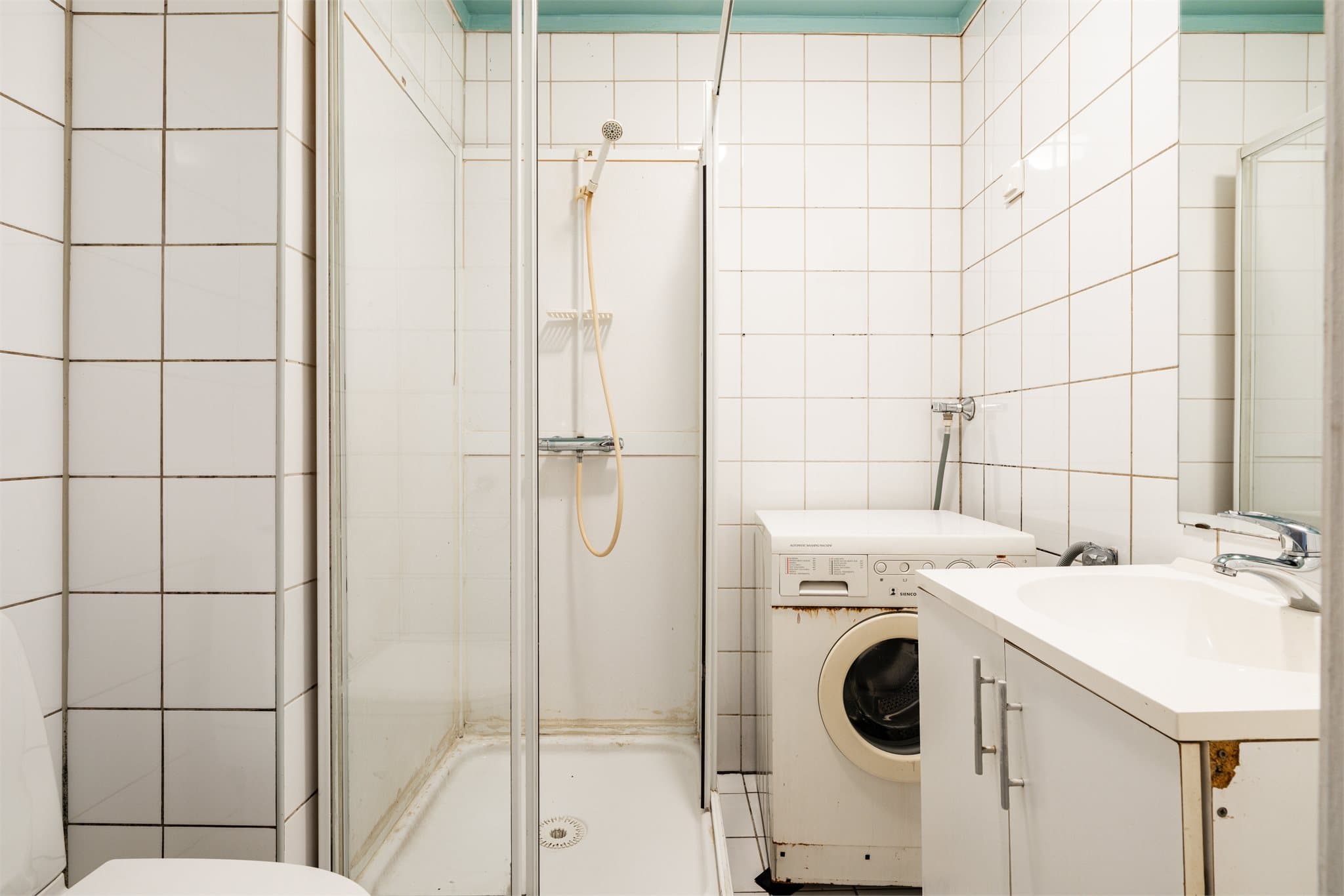 Flislagt baderom med servant med innredning, dusjkabinett og toalett.