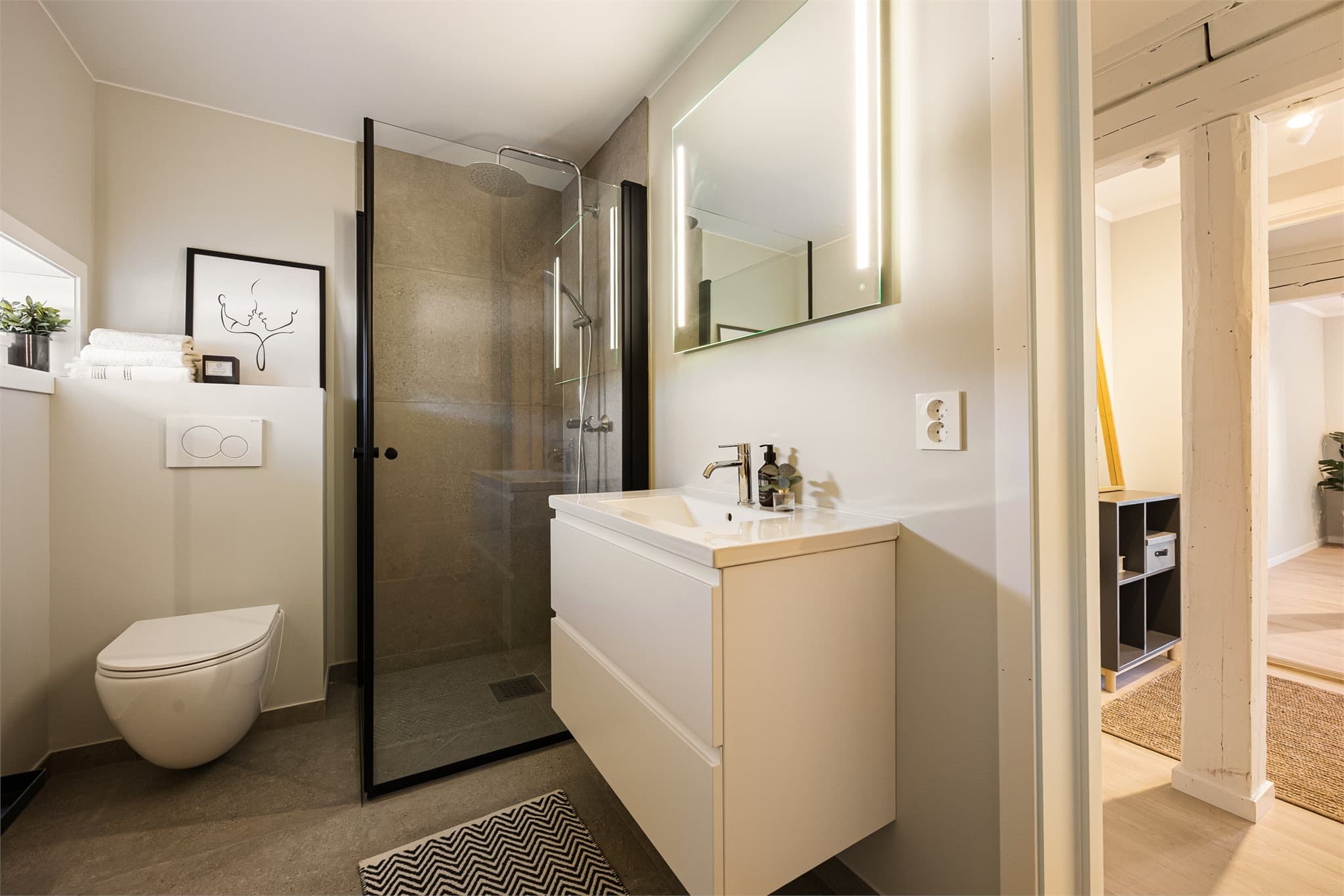 Pent baderom innredet med helservant på skuffeseksjon, vegghengt toalett og dusjhjørne med regnfallsdusj. Badet har gulvvarme.