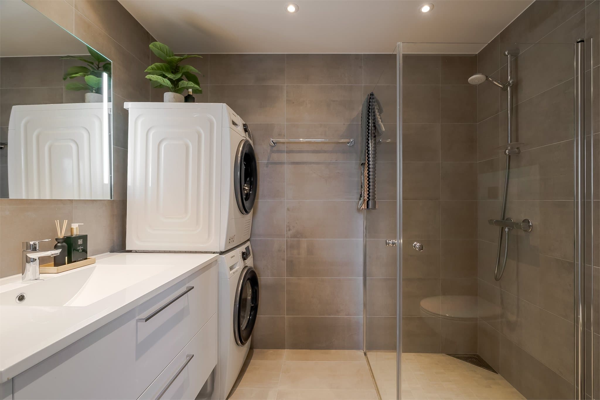 Lekkert baderom utstyrt med stor servantinnredning, speil med lys, toalett, dusjhjørne med innfellbare dusjdører og opplegg for vaskemaskin.