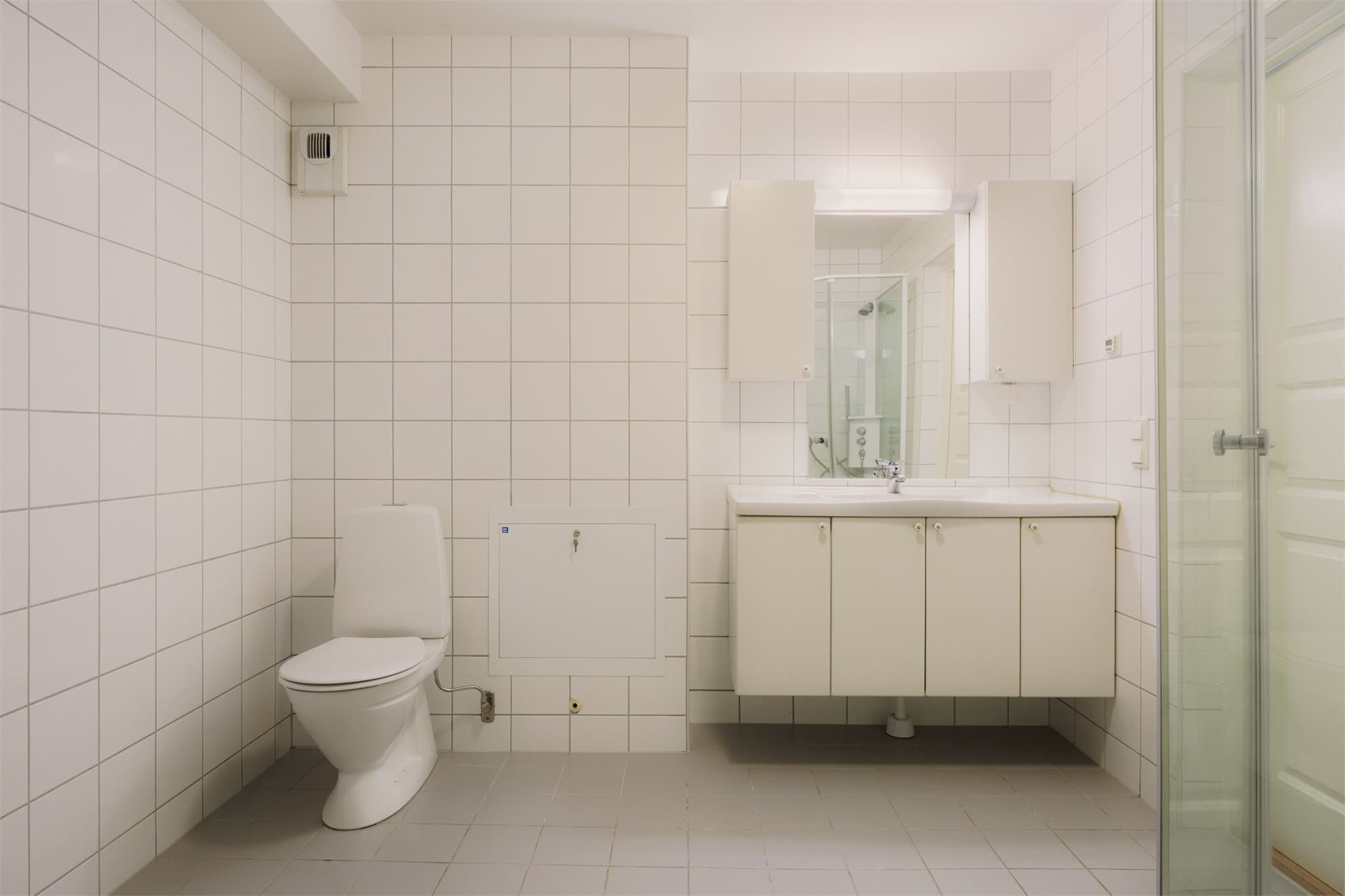 Helfliset, tidløst baderom som er innredet med servant, gulvstående toalett, dusjkabinett og opplegg for vaskemaskin.