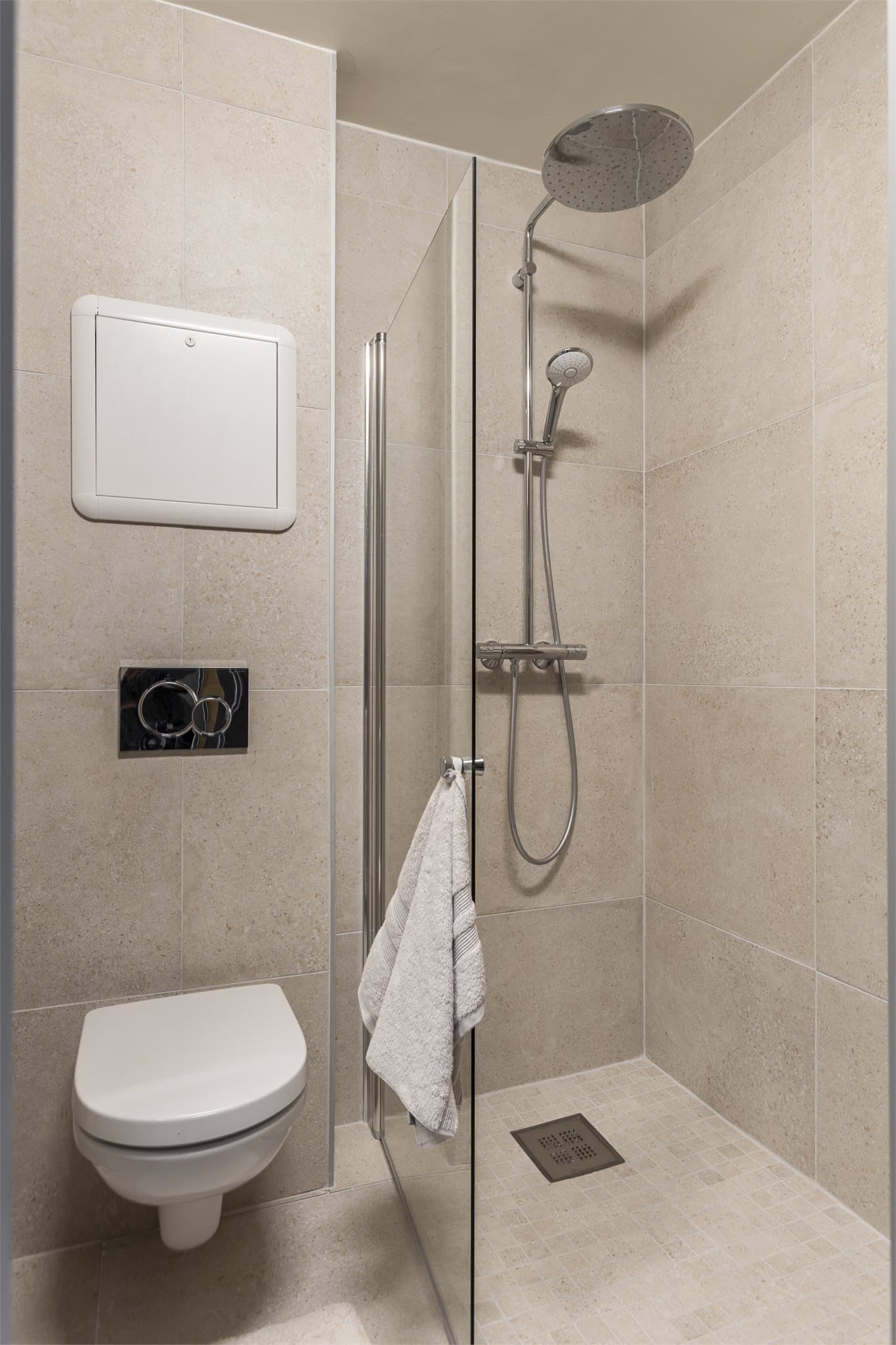 Rommet er helfliset og innredet med et dusjhjørne med glassdør og et vegghengt toalett.