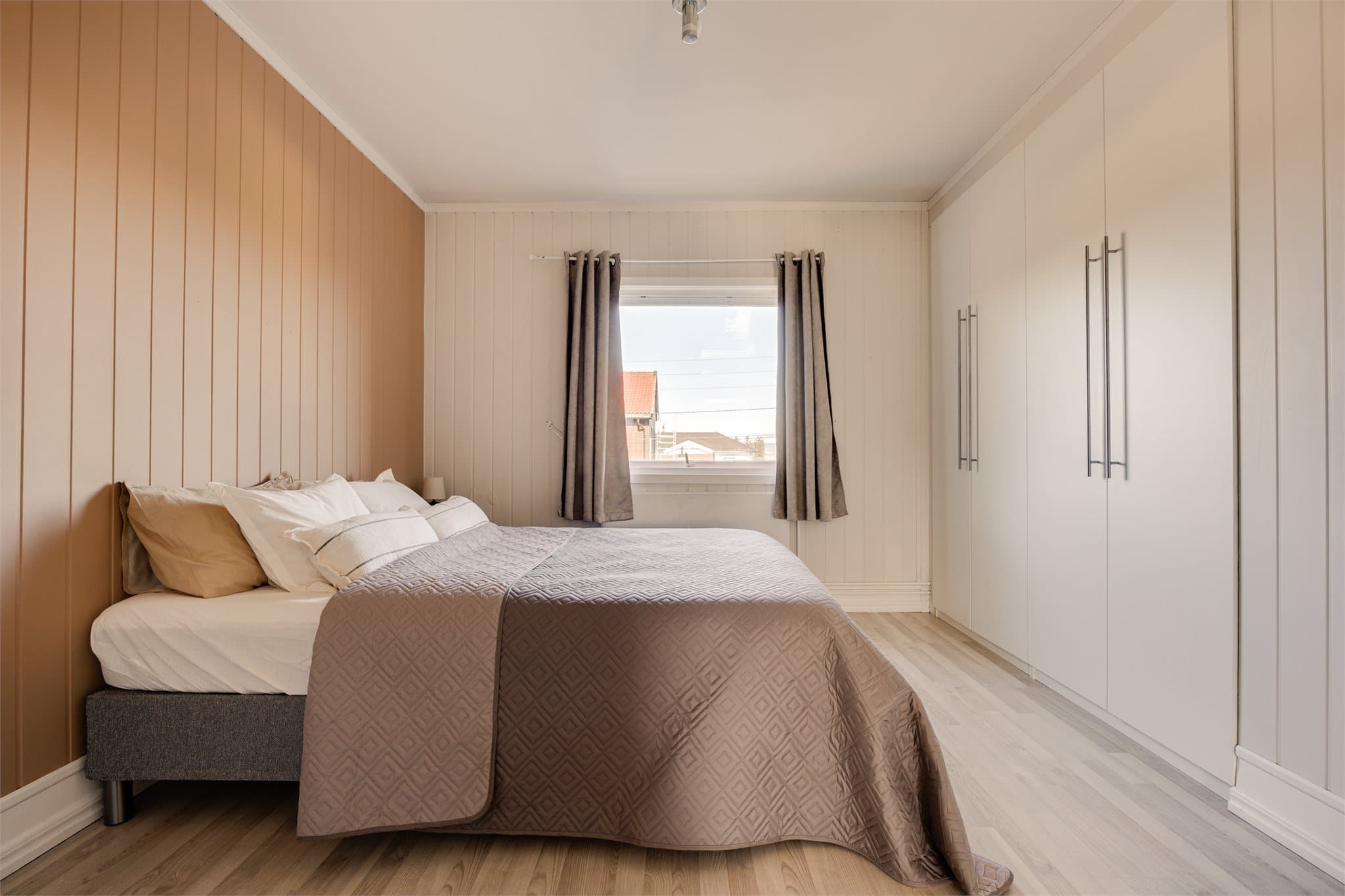 Hovedsoverommet har hvite vegger kombinert med en lun ferskenfarget kontrastvegg og integrert garderobeløsning som gir rikelig med oppbevaring.