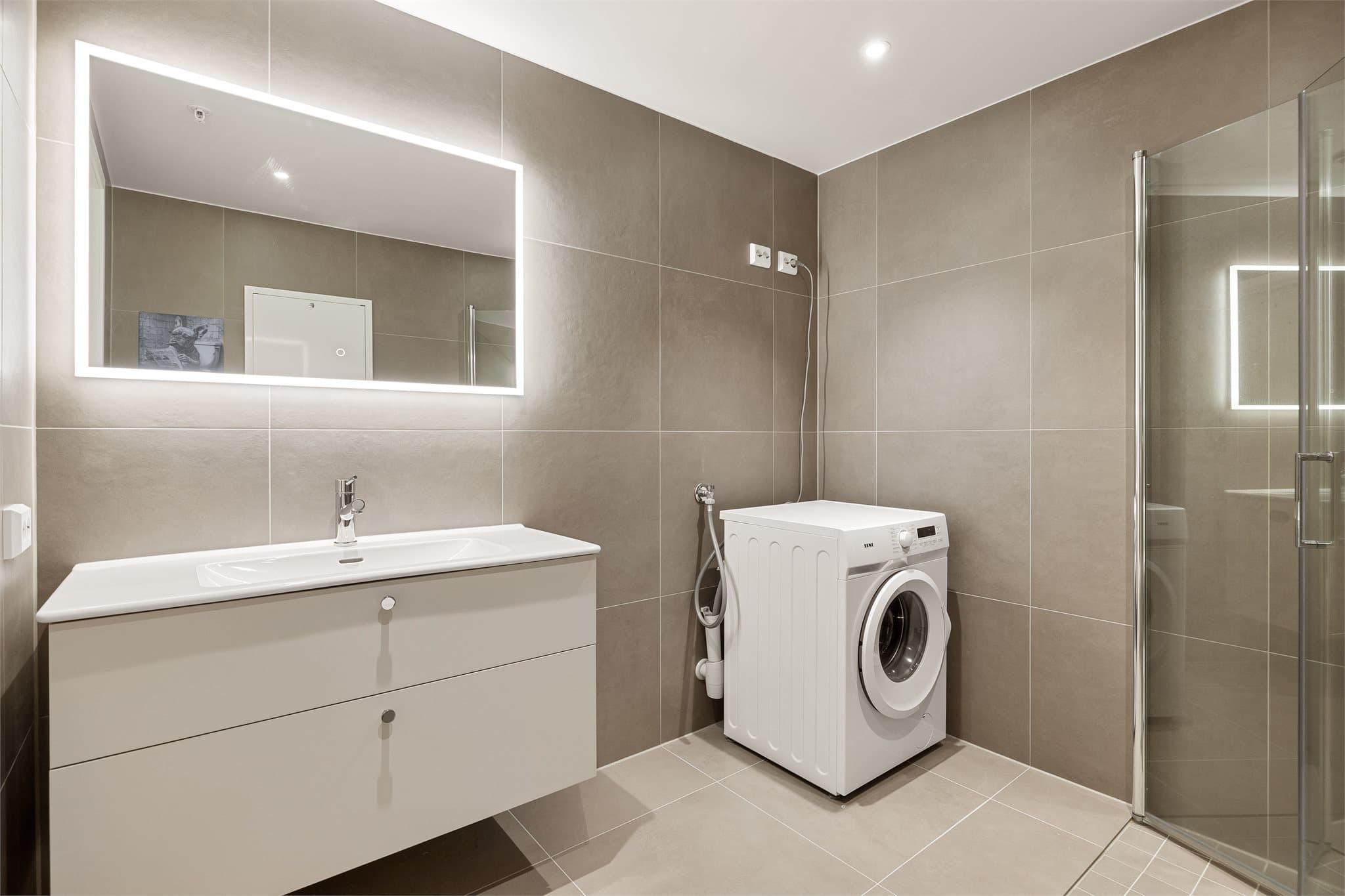 Store fliser og moderne fargetoner gir badet et stilrent og innbydende uttrykk.