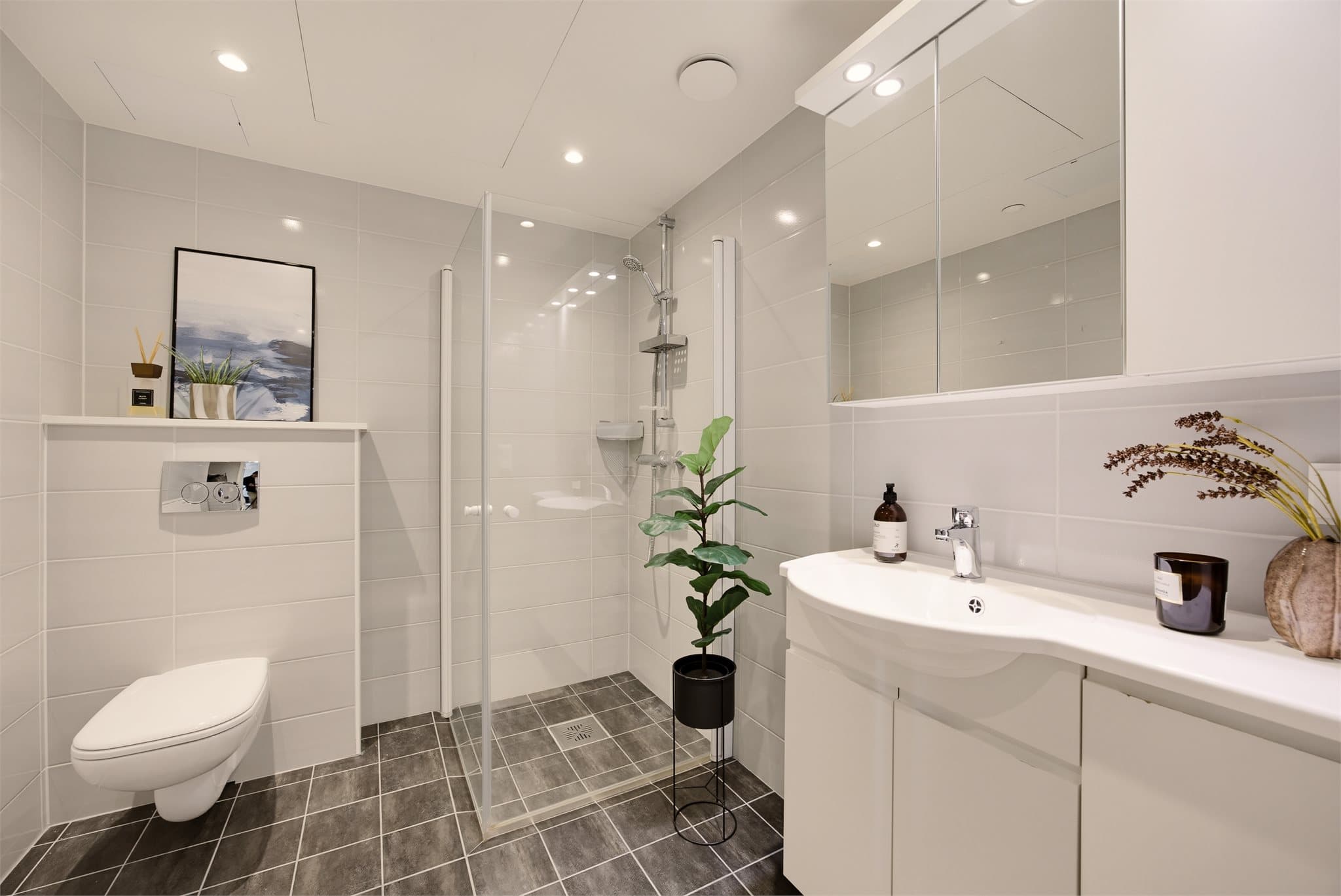 Badet har dusj med faste glassfelt og dør i herdet glass, servant, vegghengt toalett med innebygget sisterne og opplegg for vaskemaskin.