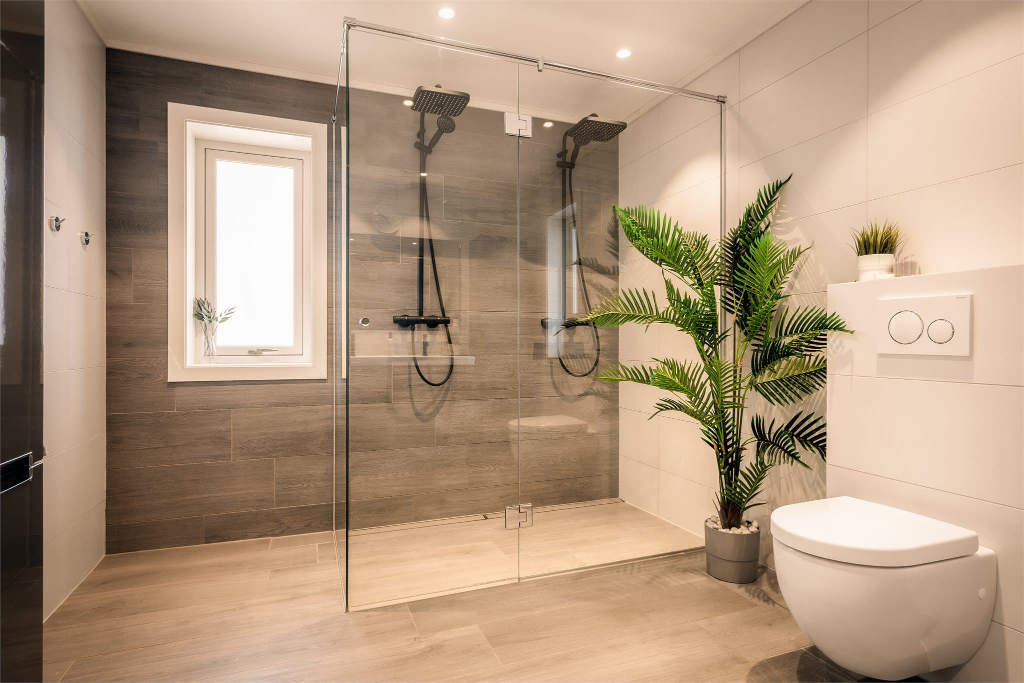 Lekkert og moderne baderom med store, elegante fliser som gir et stilrent og eksklusivt uttrykk. Den doble regnsfallsdusjen med gjennomgående sort armatur skaper en luksuriøs spa-følelse.