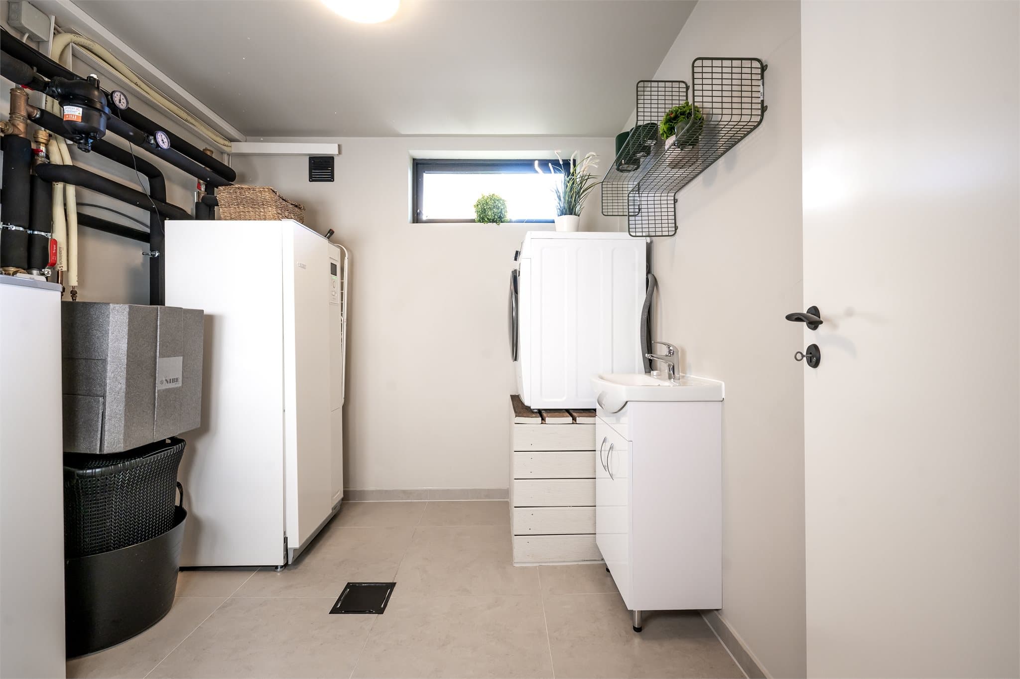 Moderne vaskerom/ bod og funksjonelt vaskerom fra 2024 med flislagt gulv, opplegg for vaskemaskin og tørketrommel, samt praktisk oppbevaring.