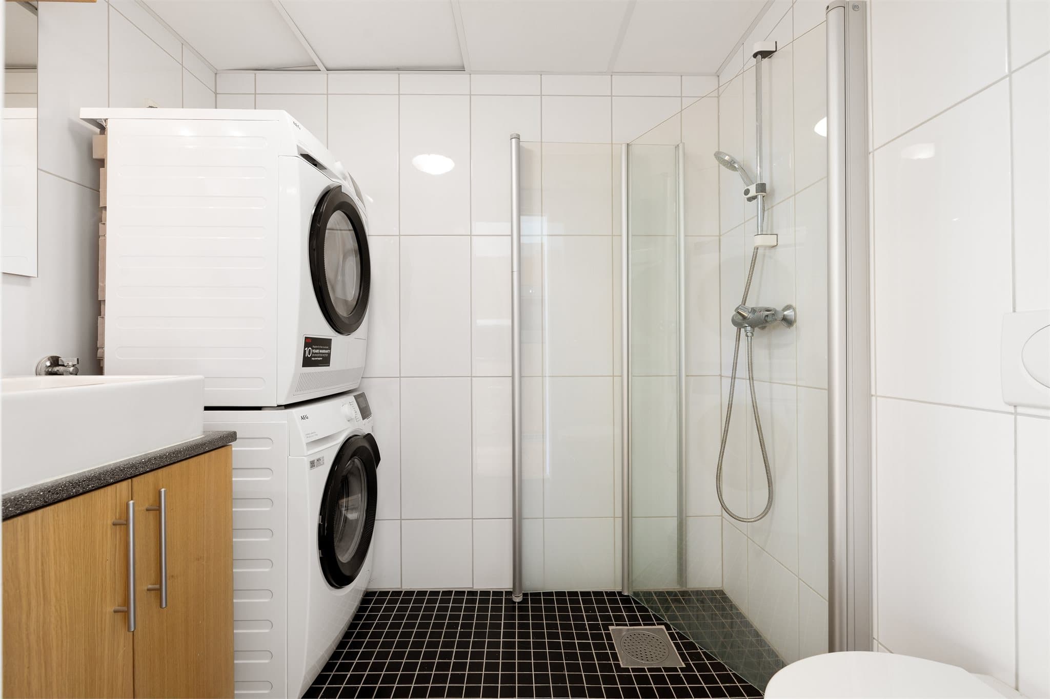 Lyst og tidløst baderom utstyrt med servantinnredning, speil, dusjhjørne og toalett.