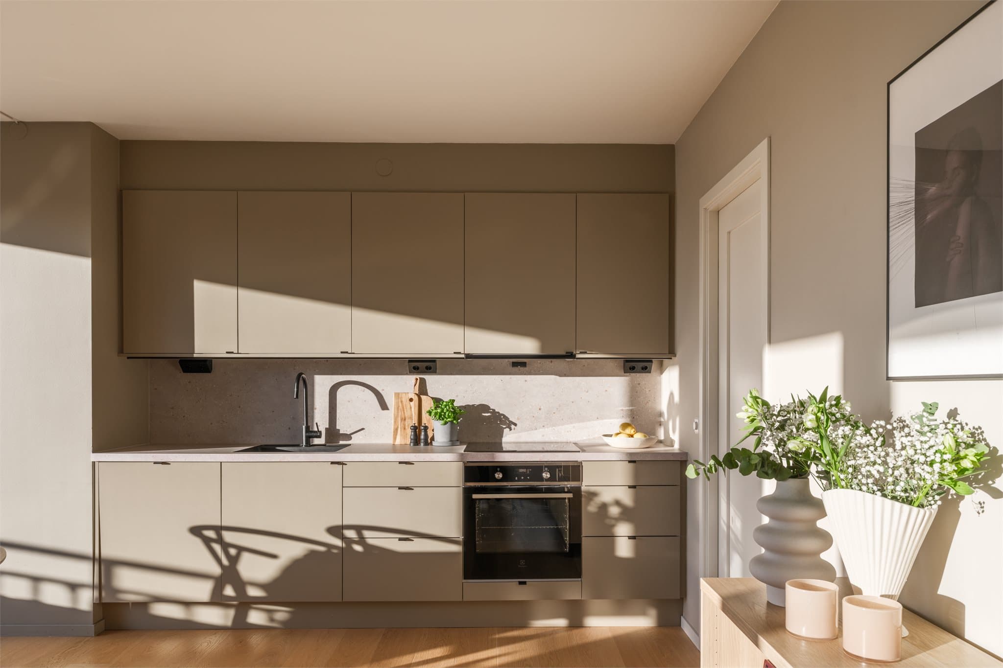 Elegant kjøkken med helt nye fronter fra 2025 og en lekker benkeplate som sømløst fortsetter opp langs veggen for et moderne og gjennomført uttrykk.