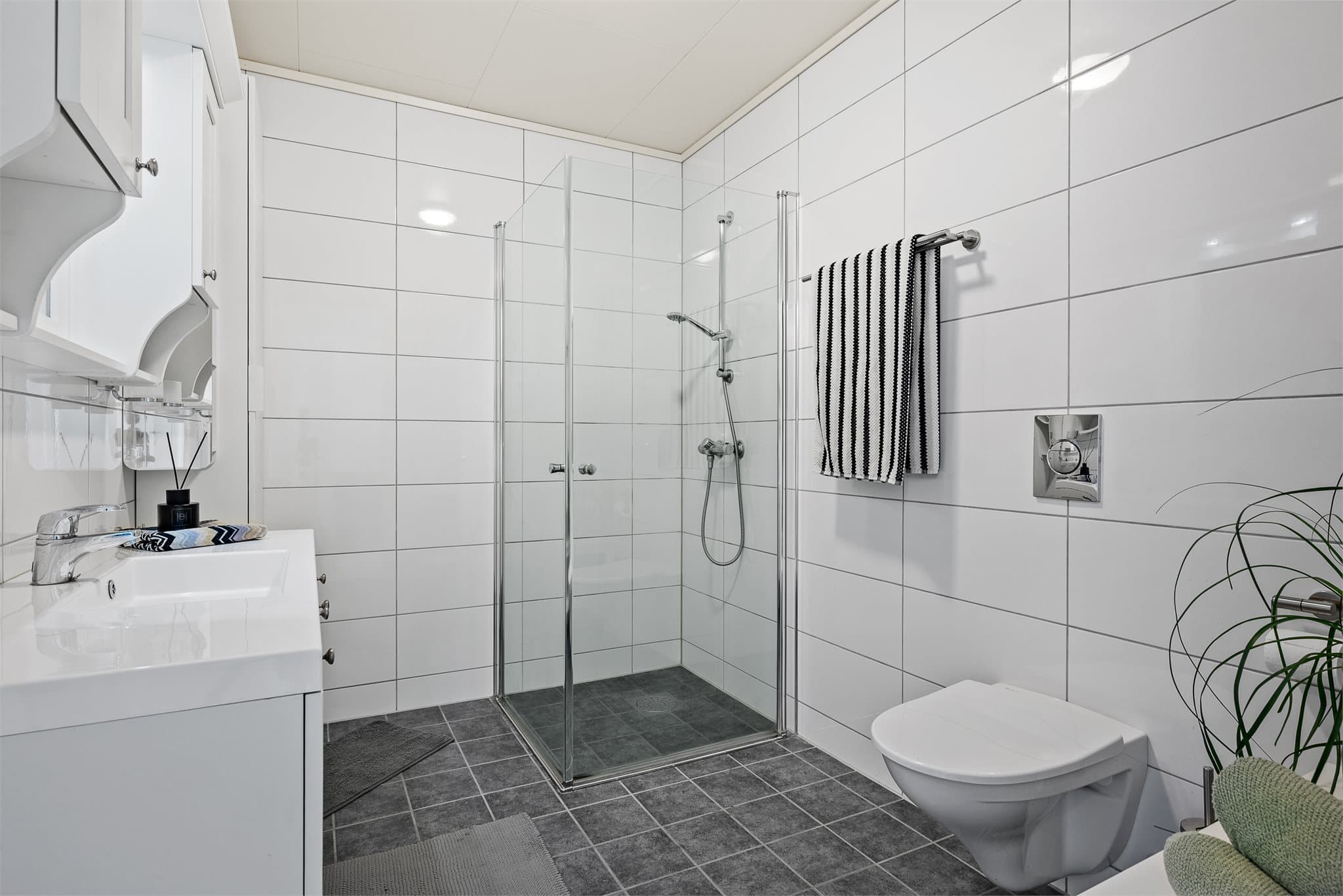 Badet er utstyrt med servantinnredning, dusjhjørne og vegghengt toalett.