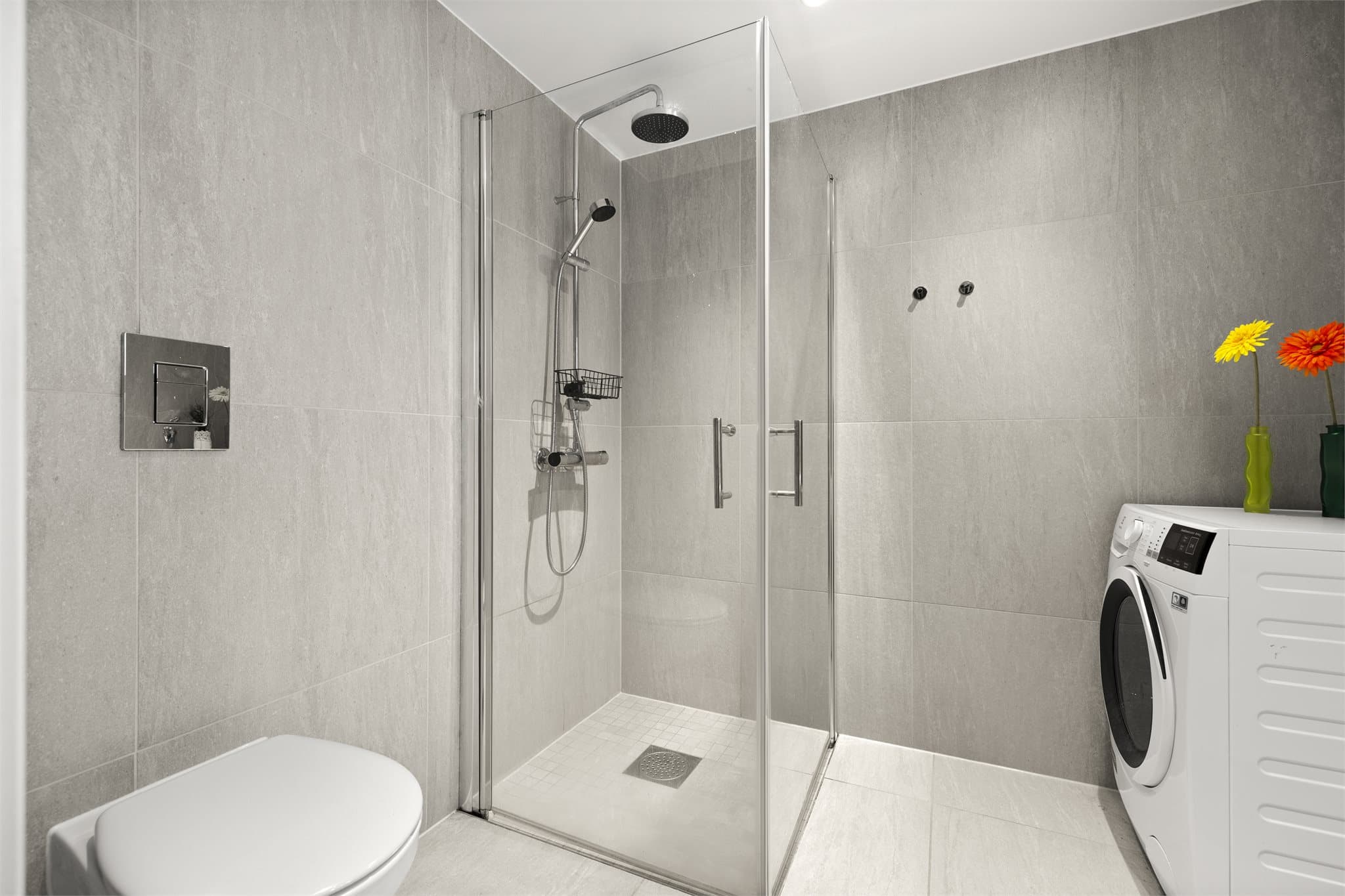 Bad med dusjløsning i glass og veggmontert toalett.