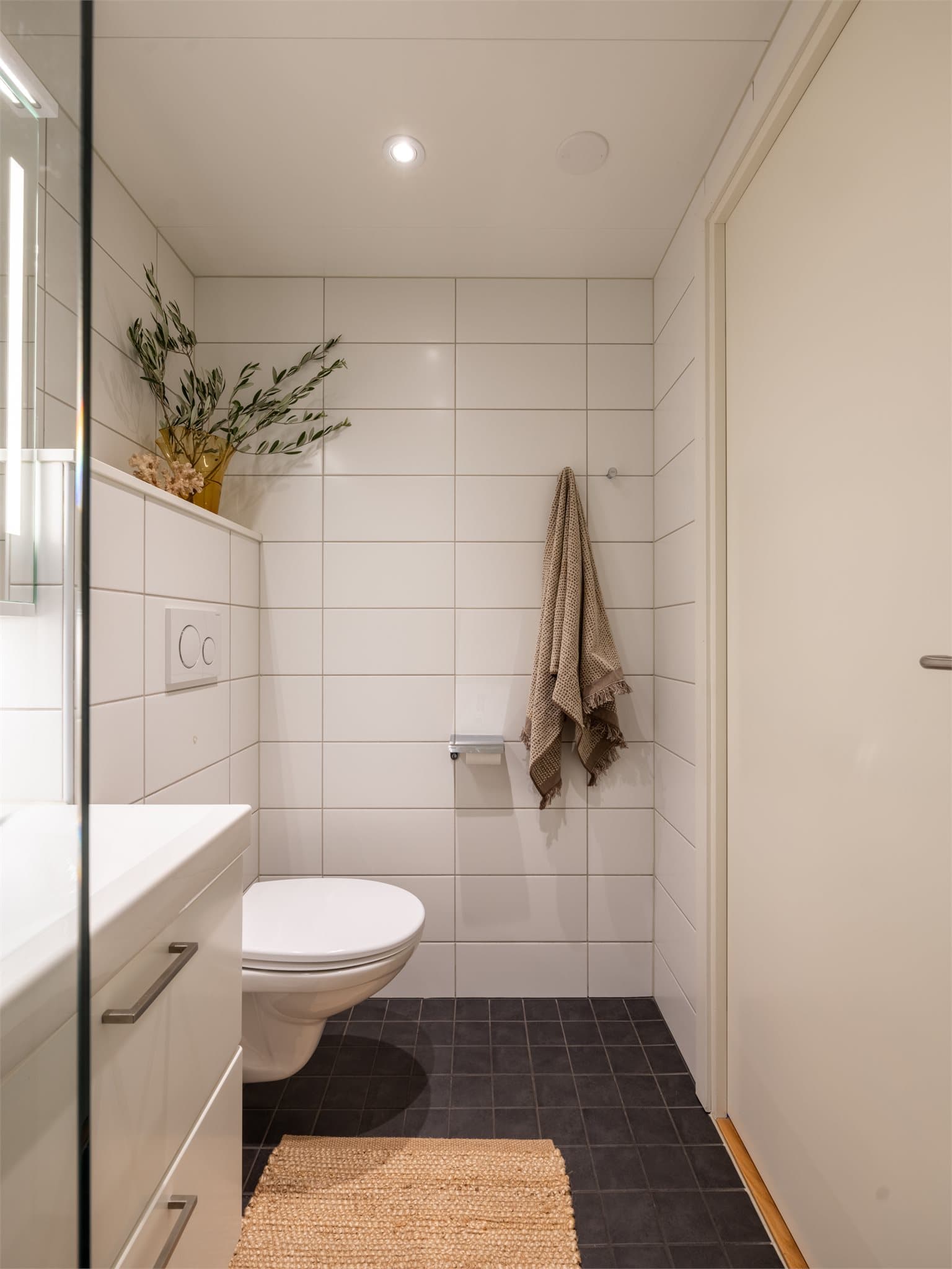 Baderommet er stilrent innredet med servant og skap, speil, høyskap, vegghengt toalett og dusjhjørne med glassdører.