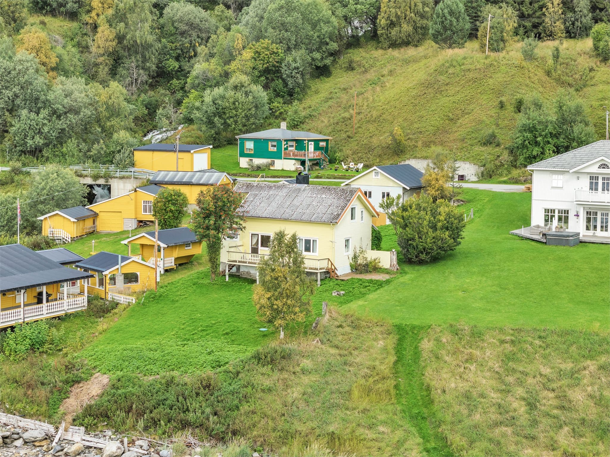 Tunet rommer både fritidsbolig og uthus (gammelfjøsen) i skrånende terreng ved fjorden