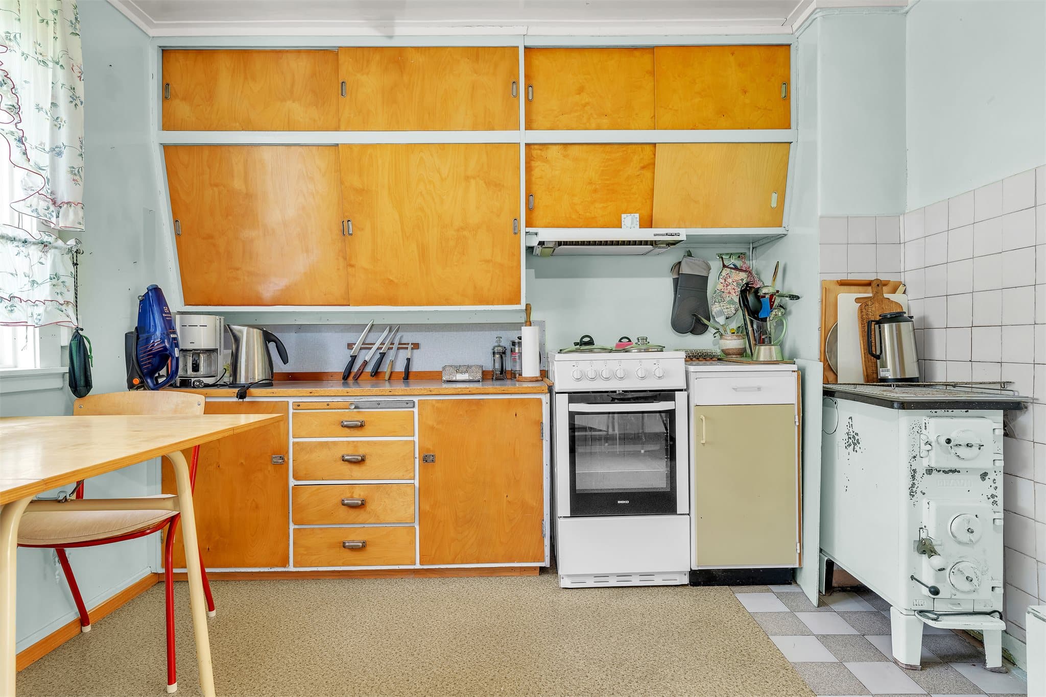 Kjøkkenvegg med over- og underskap, komfyrplass og ventilator med avtrekk.