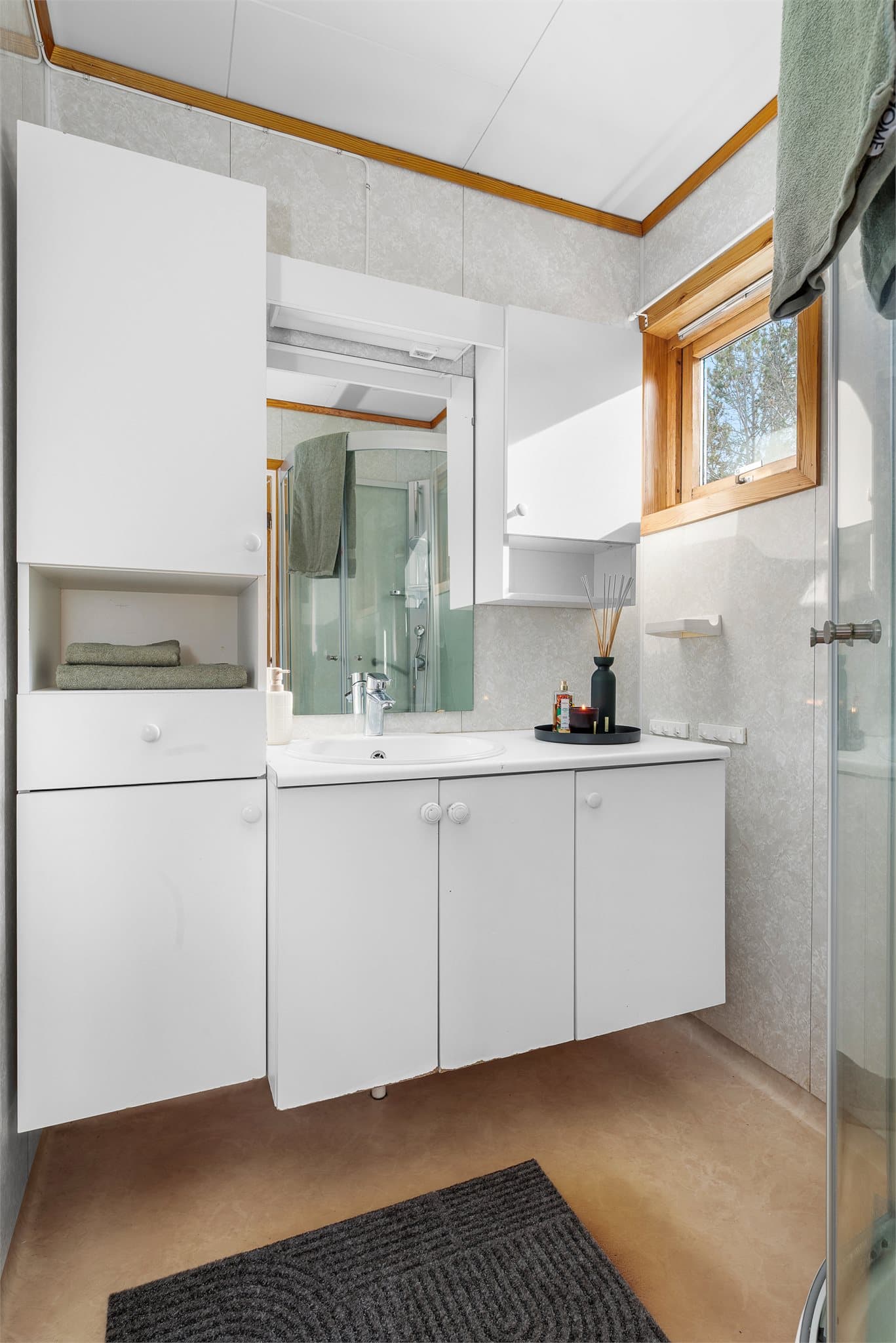 Badet er utstyrt med servantinnredning, skap, dusjhjørne og toalett.