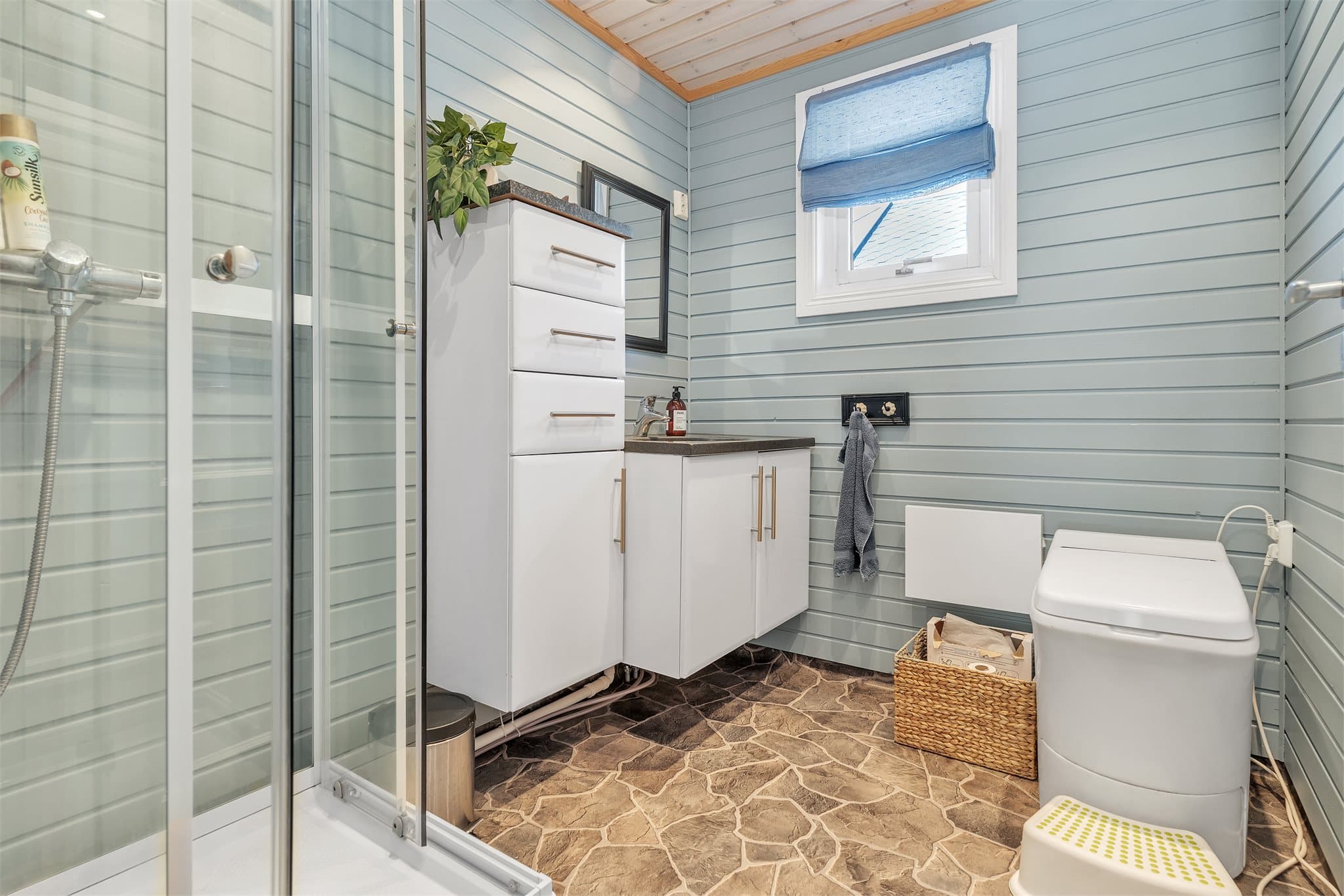 Badet er utstyrt med forbrenningstoalett, dusjkabinett og servantinnredning.