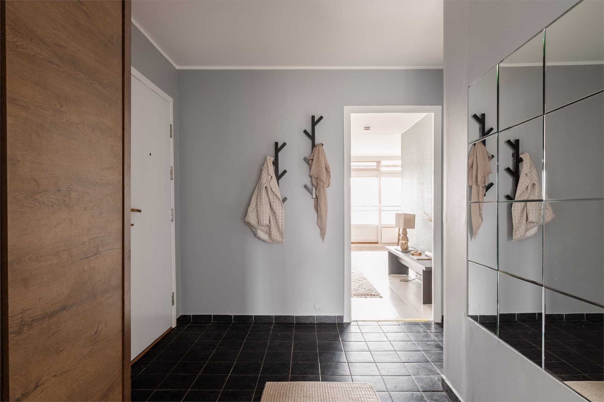 Hallen har flislagt gulv og leder videre inn mot stuen og leilighetens sosiale sone.