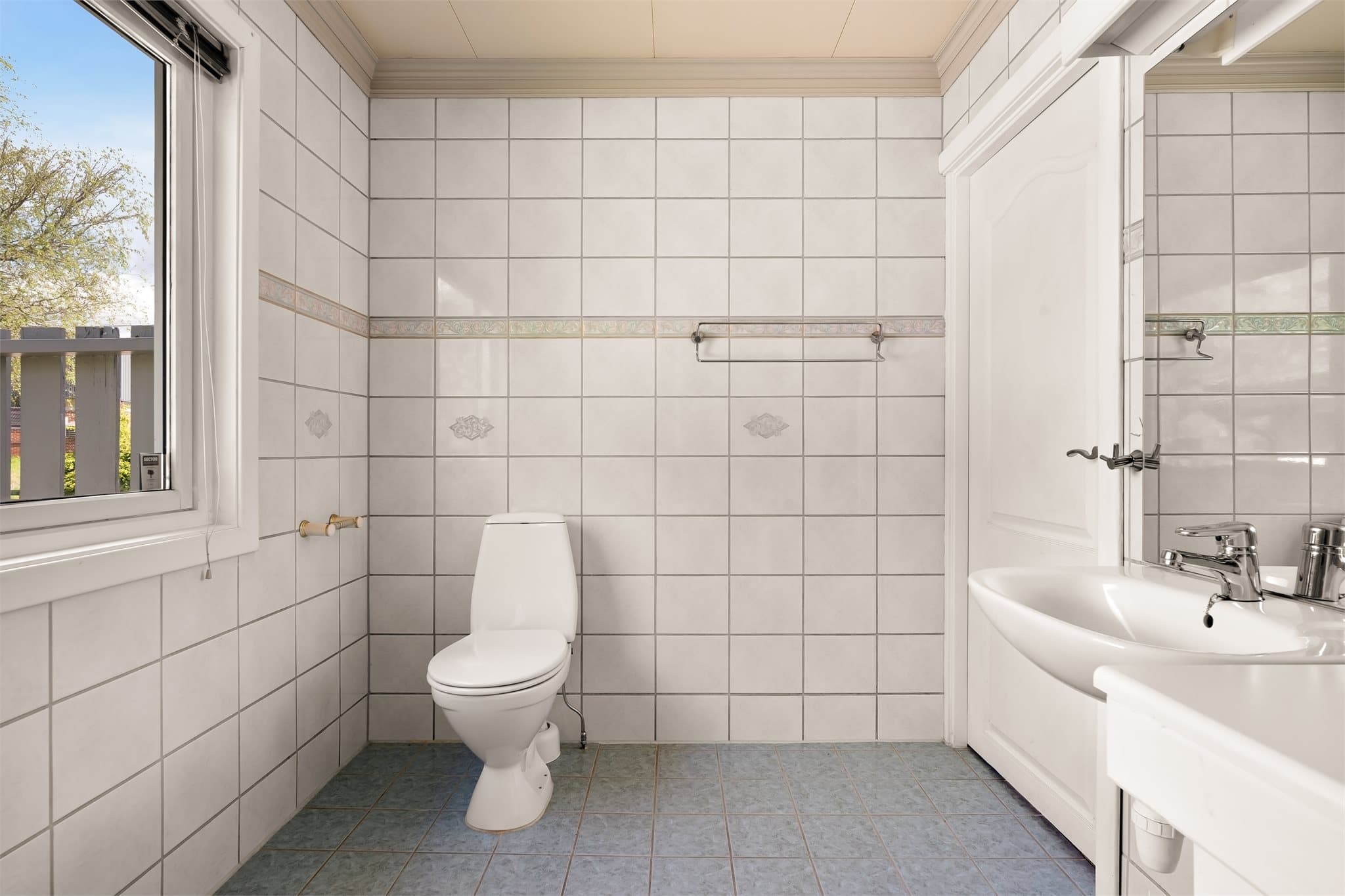 Badet er innredet med servant, speil med tilhørende belysning, dusjhjørne med glassdører og gulvmontert wc.