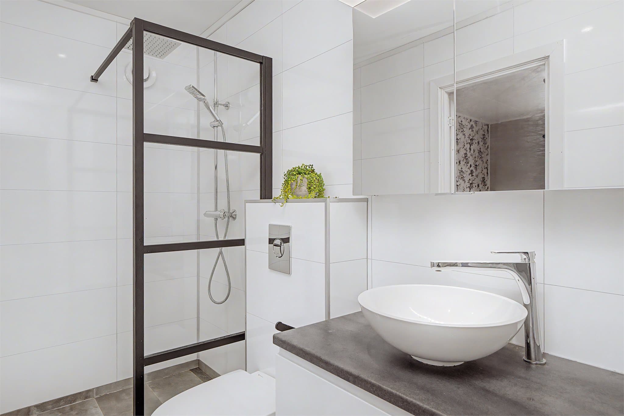 Dusjhjørne med stilrene glassvegger og en moderne servantinnredning. Ventilasjon skjer via elektrisk styrt vifte.