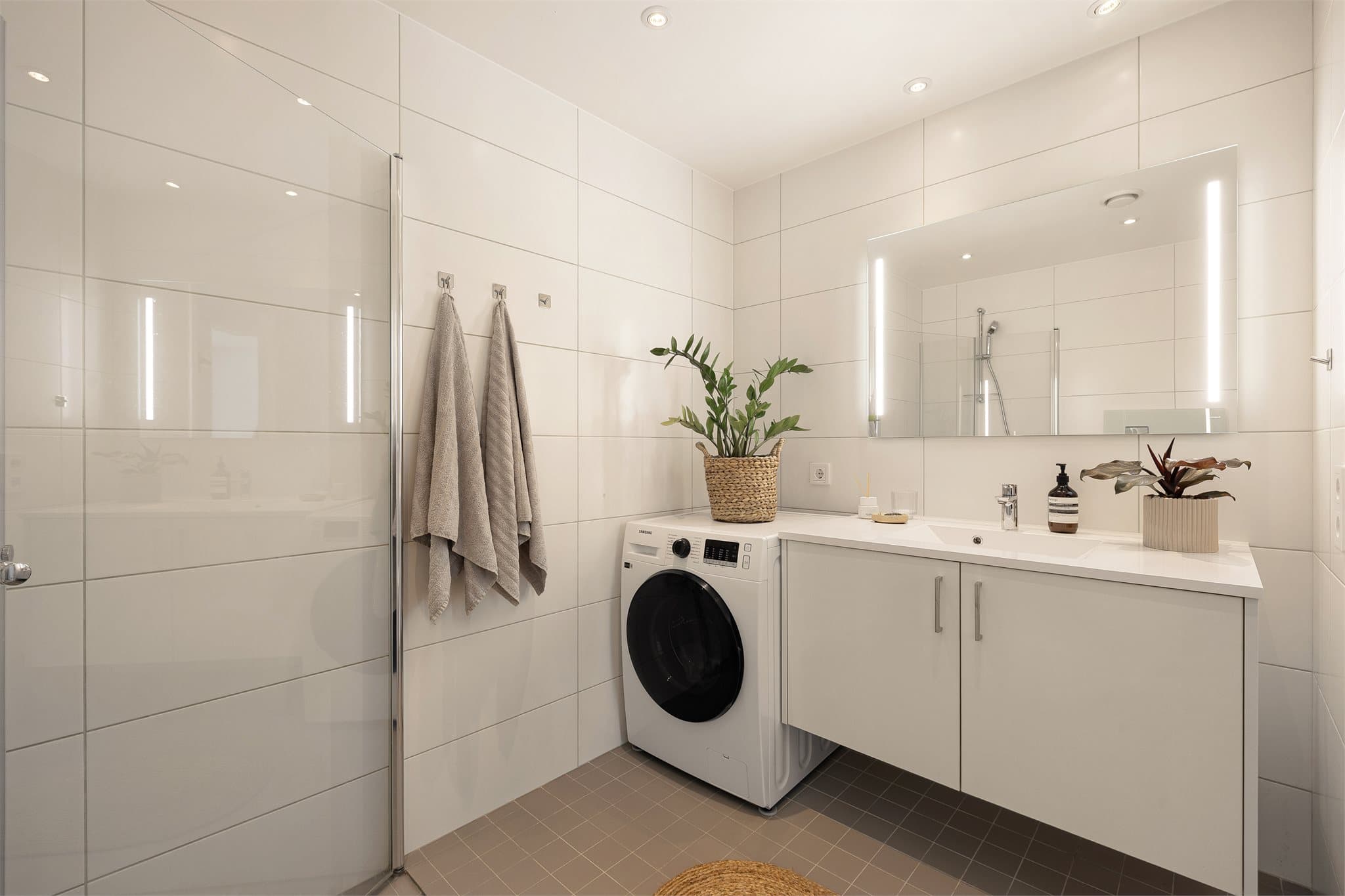 Badet er moderne og innredningen består av servant med skap, vegghengt toalett og dusjhjørne med innfellbare dører.