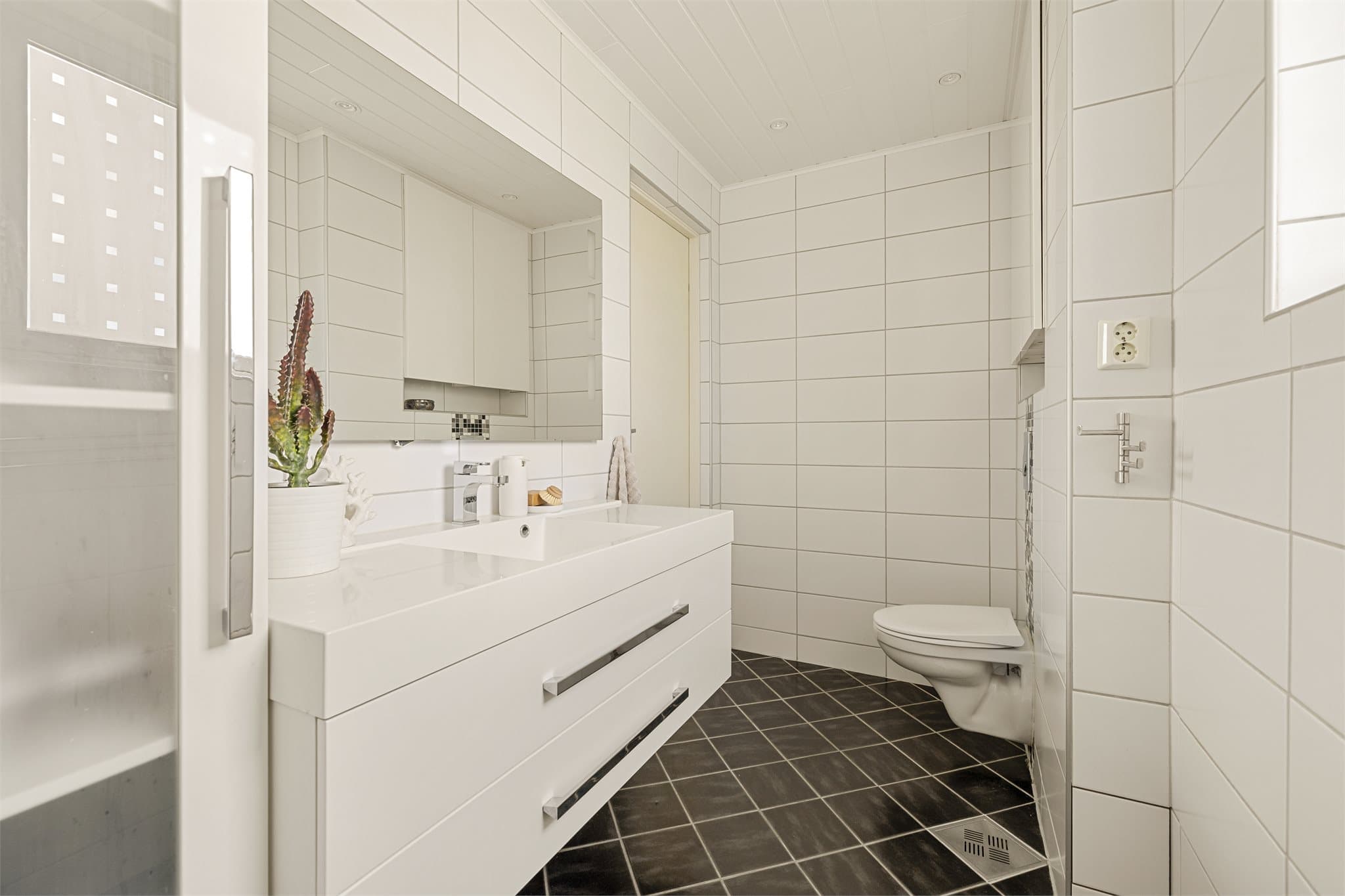 Det er utstyrt med dusjnisje med skyvedør, regnfallsdusj og termostatstyrt blandebatteri, veggmontert toalett samt servantskap med heldekkende servant og speil med belysning.