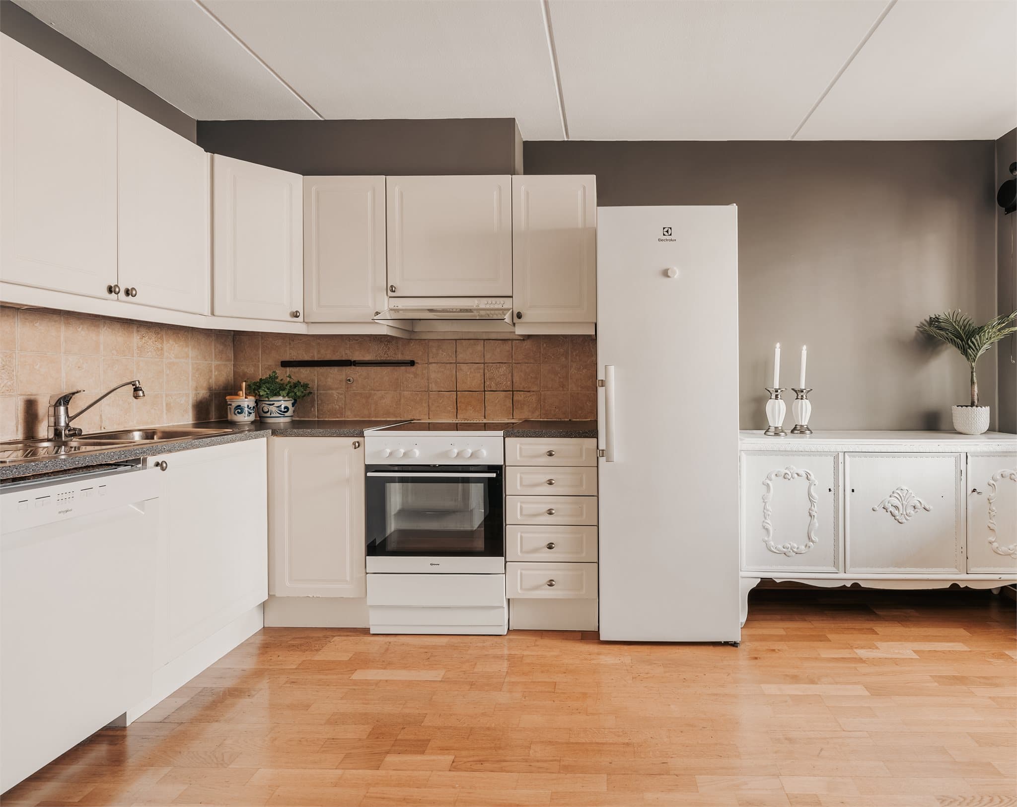 Kjøkkeninnredning fra byggeåret. Innredning med profilerte, fabrikklakkerte fronter og benkeplate i laminat med nedfelt kum i rustfritt stål. Det er fliser over benkeplate.