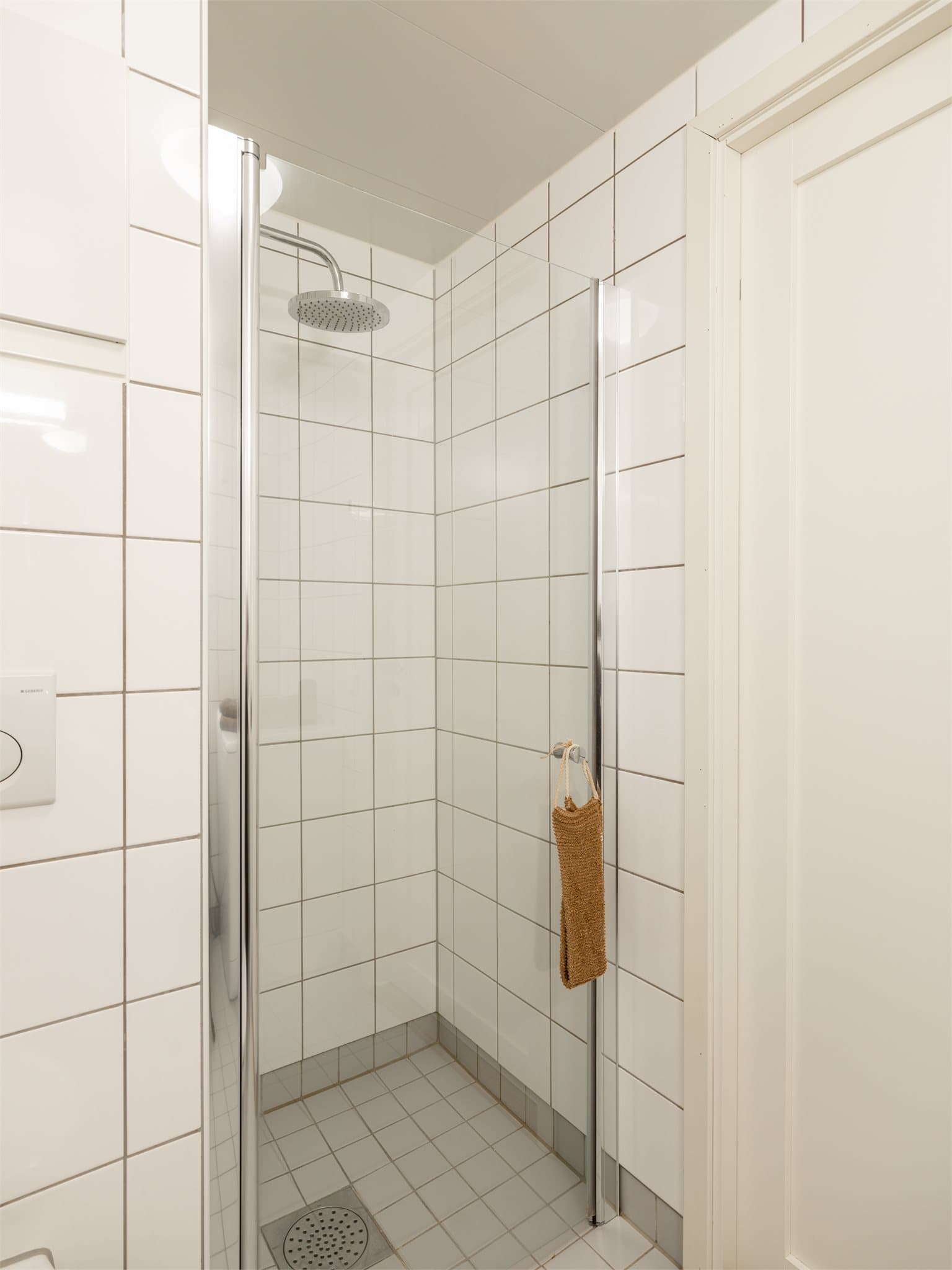 Badet er innredet med vegghengt toalett, servant nedfelt i innredning med tilhørende speil, samt dusjhjørne med svingbare glassdører.