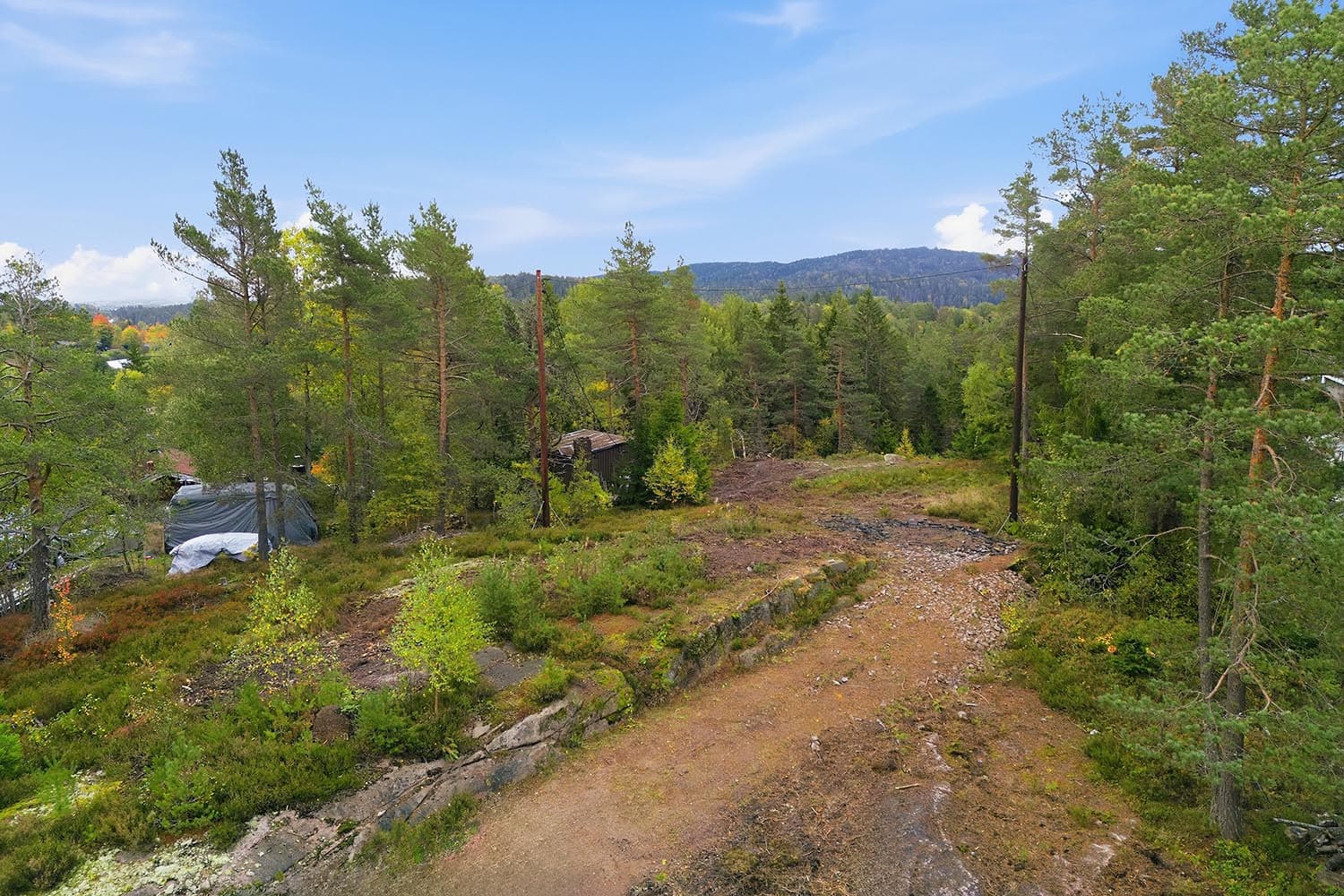 Tomten ligger fint til i terrenget, omgitt av skog og vakker natur. Eier har i sin eiertid felt flere trær på eiendommen og laget innkjøring inn på tomten.