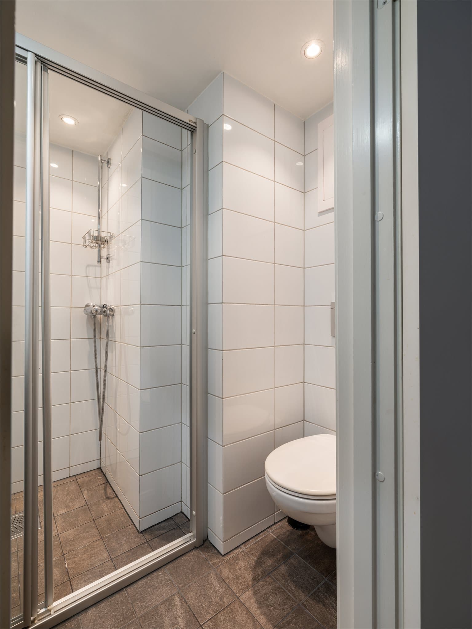 Badet er innredet med vegghengt toalett, servant innredning på skuffeseksjon og dusj på vegg.