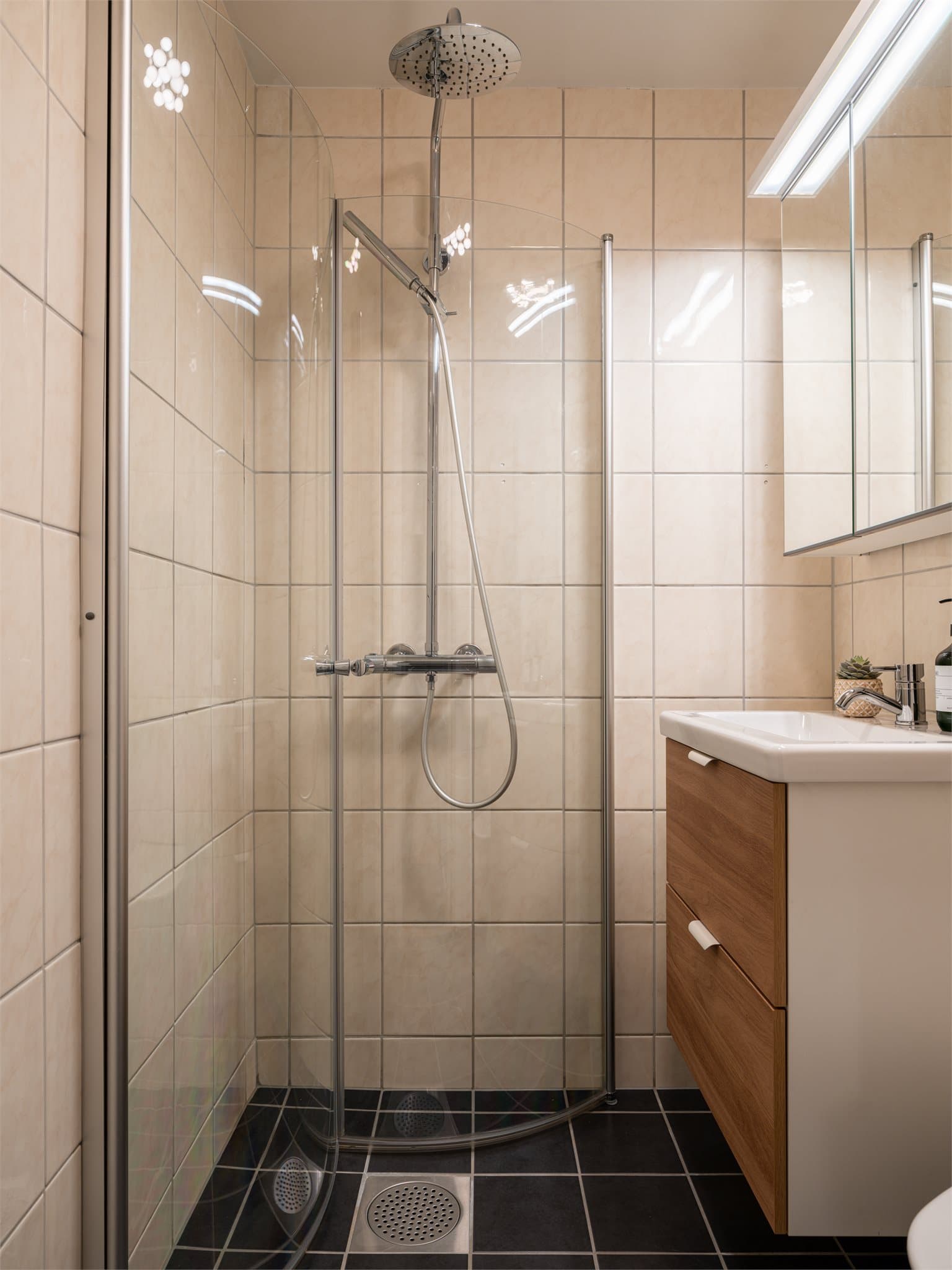 Badet har en praktisk innredning med servant, skuffeseksjon, speil med belysning og skap som gir gode oppbevaringsmuligheter.