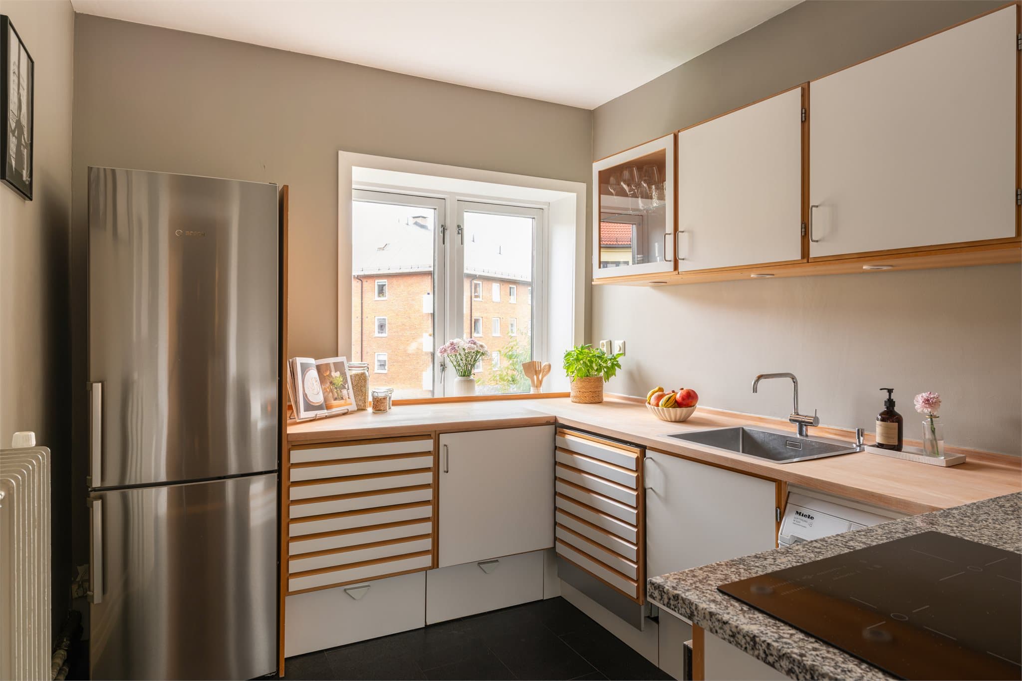 Separat koselig kjøkken innredet med skapinnredning, vitrineskap og benkeplate i laminat og stein.