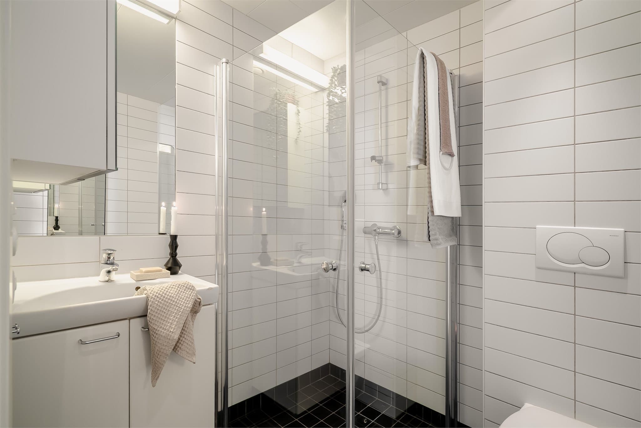 Lyst og tidløst baderom med hjørnedusj, servantinnredning og toalett.