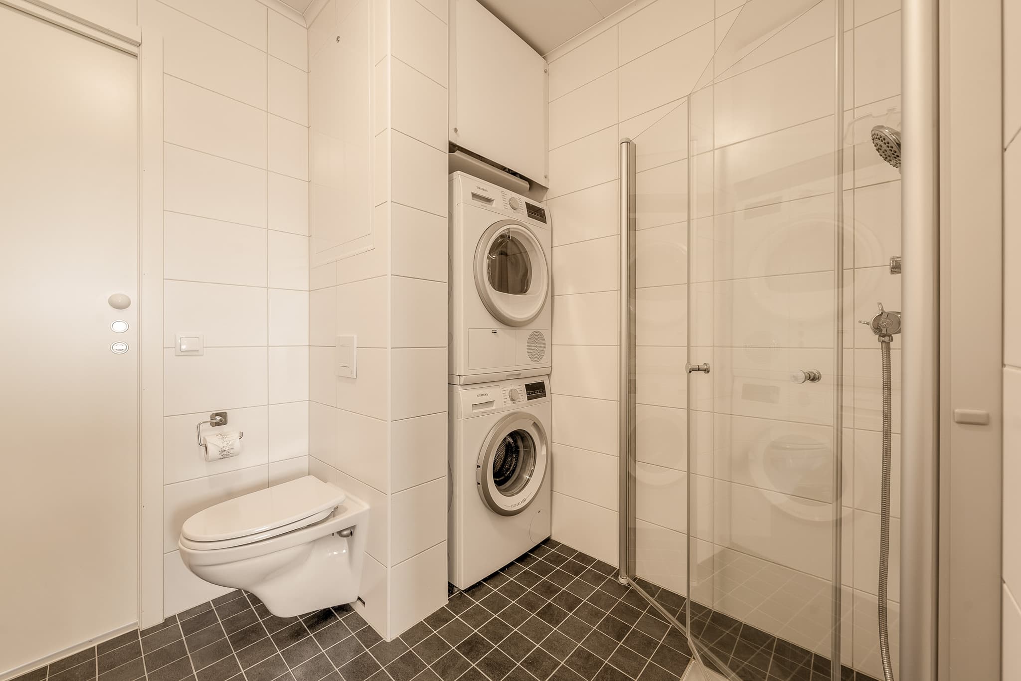 Videre er det vegghengt toalett, dusjhjørne og egen nisje med plass til vaskemaskin og tørketrommel.