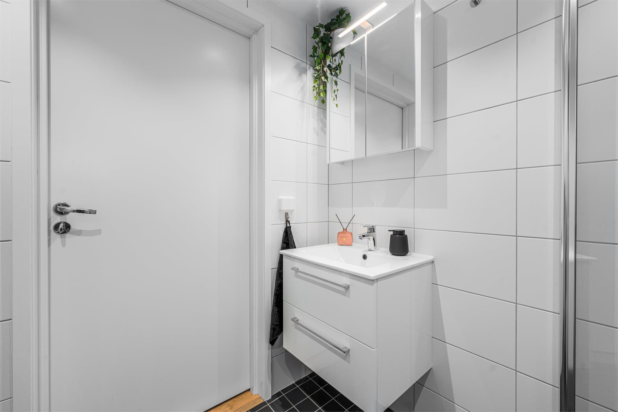 Badet er innredet med helservant på skuffeseksjon, dusjhjørne og vegghengt toalett.