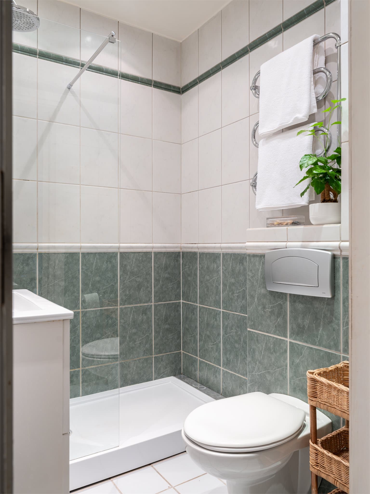 Badet er innredet med vegghengt toalett, servant med underskap og dusjhjørne.