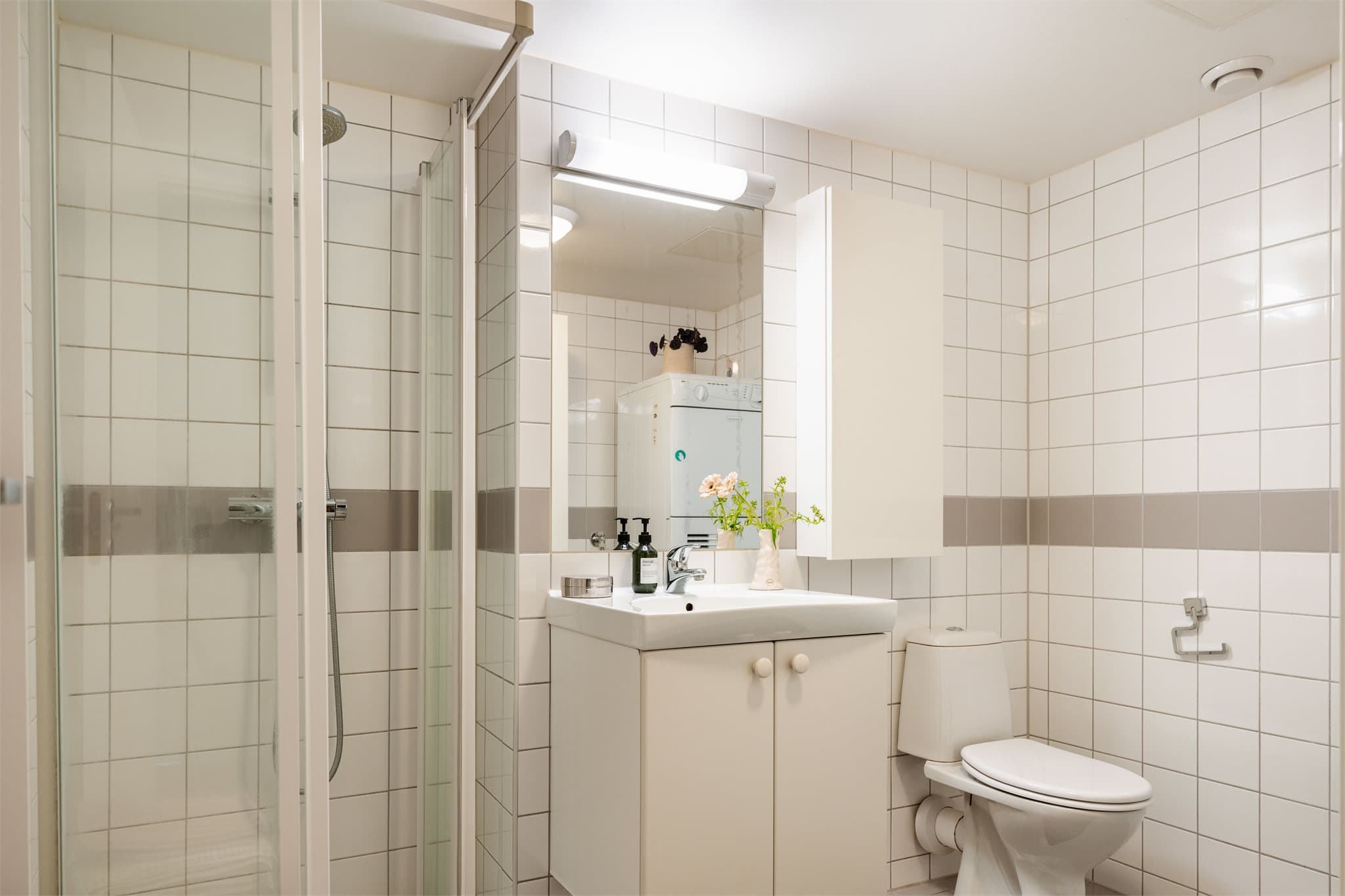 Dusj på gulv med dusjdører i herdet glass, servant med praktisk skapinnredning og frittstående toalett.