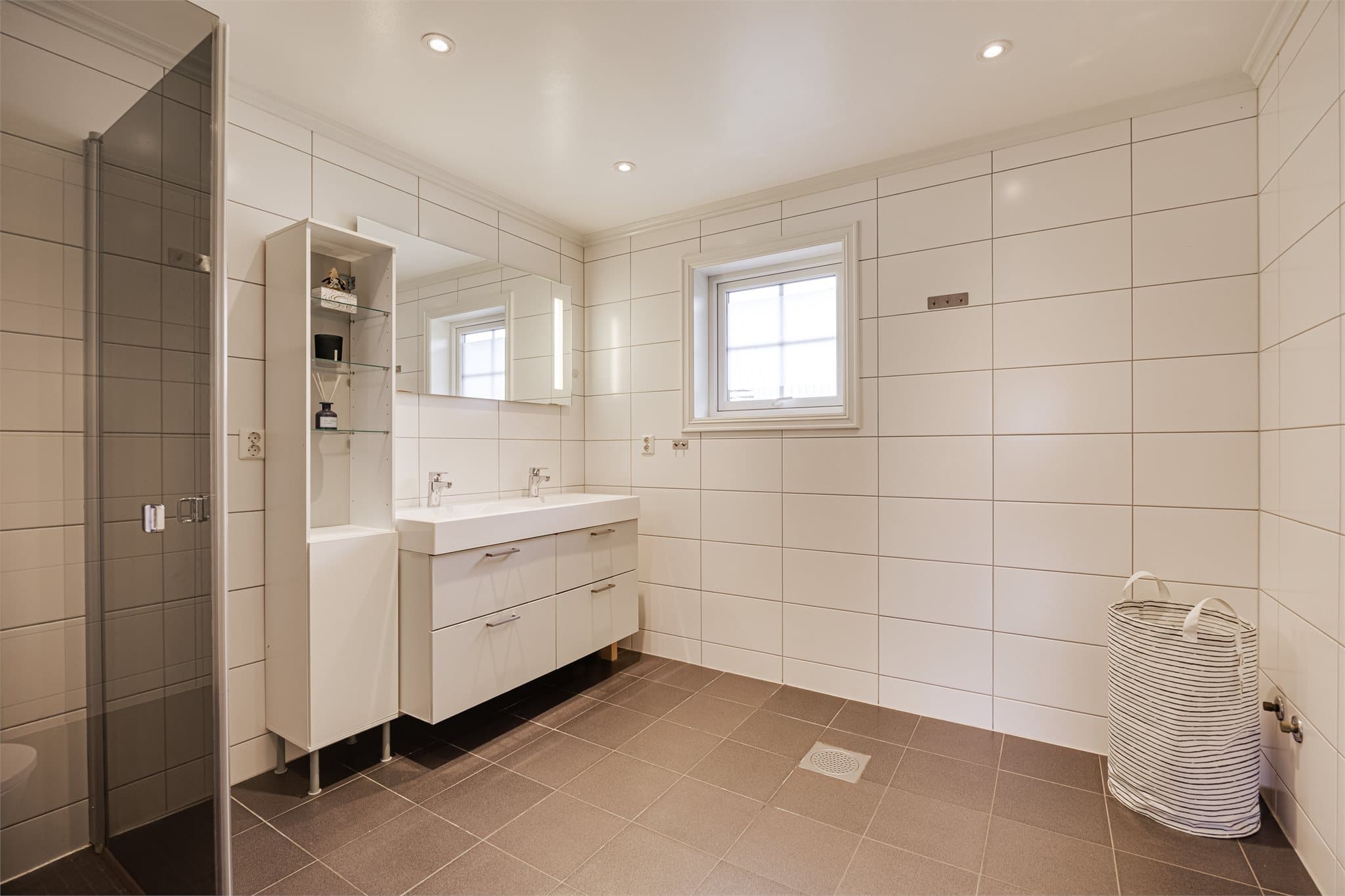 Romslig, helfliset baderom med dusjhjørne, toalett og dobbel servant.