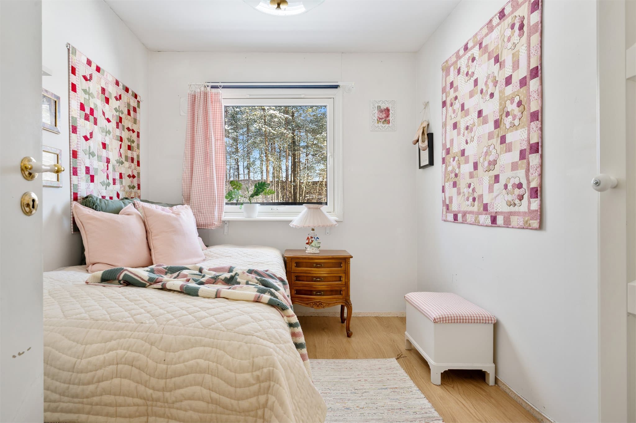 Tilbaketrukket: Soverom nr. 2 er et lyst og sjarmerende rom med lysmalte vegger som gir en luftig og behagelig atmosfære. Veggen prydes av kreative lappetepper, som tilfører personlig preg, farger og varme, og gjør rommet unikt og innbydende.