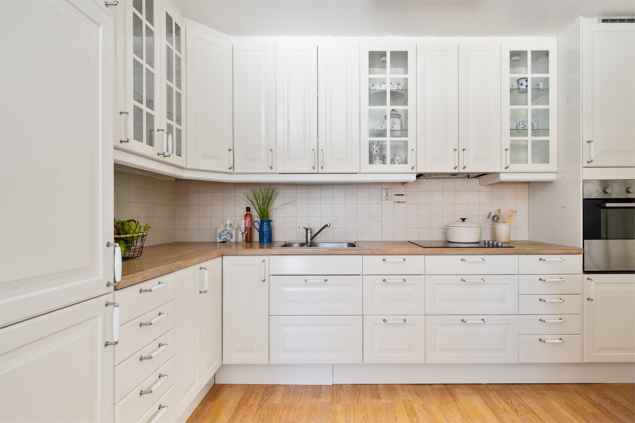 Gastronomisk spillerom: Innredningen er fra IKEA (ca. 2012) og har hvite, profilerte fronter som gir et tidløst og klassisk uttrykk. Vitrineskapene tilfører et elegant preg og gir mulighet for å vise frem servise og glass på en dekorativ måte.