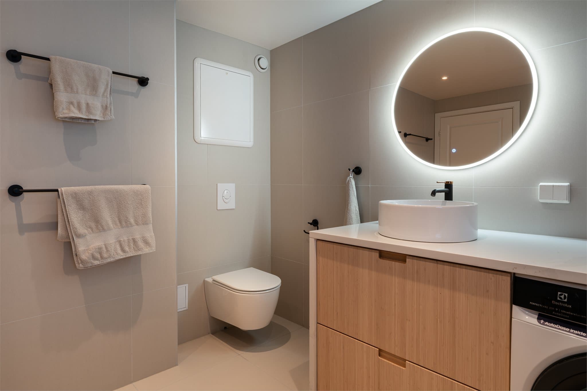 Speil med integrert belysning og et vegghengt toalett med skjult sisterne.